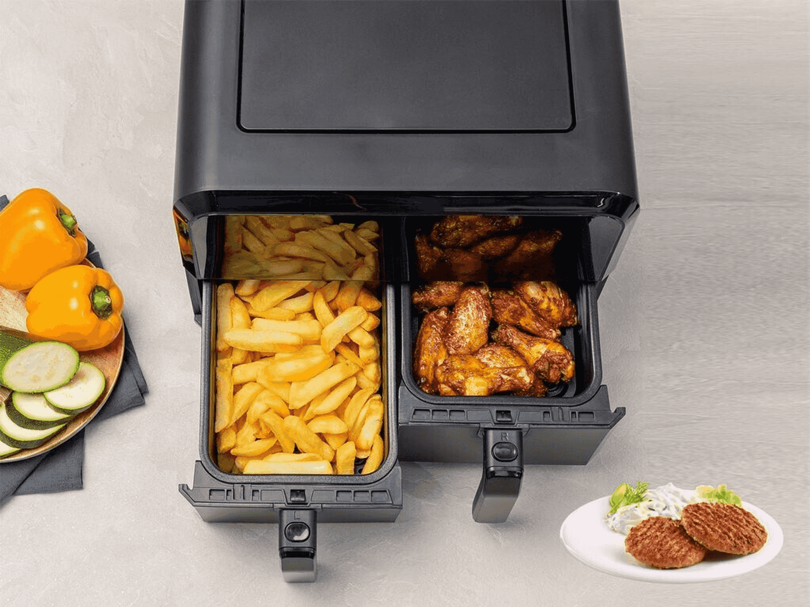 Freidora de aire de doble cesta con patatas fritas a la izquierda y alitas a la derecha.