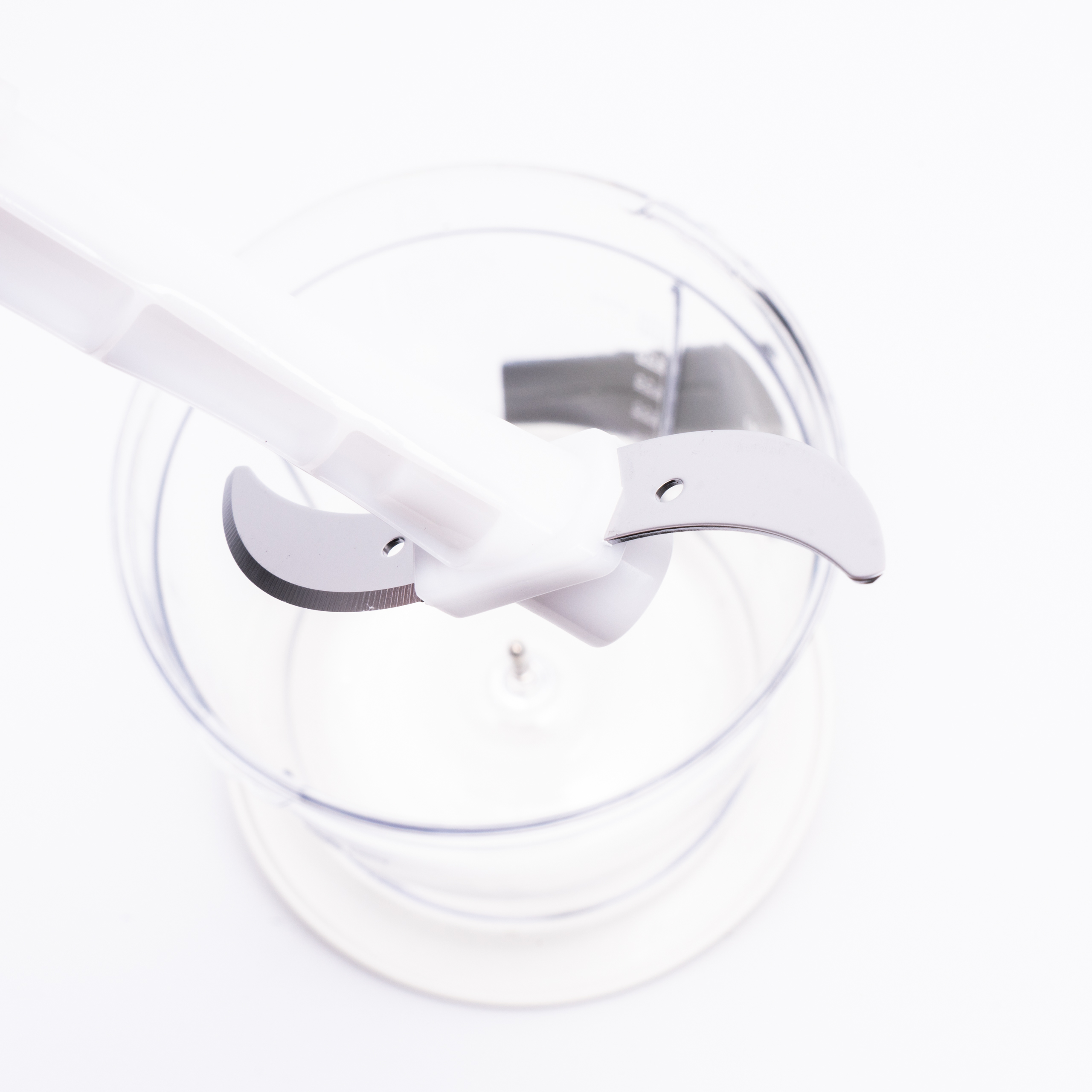 Edelstahlmesser eines Zerkleinerers über einem transparenten Plastikbehälter.