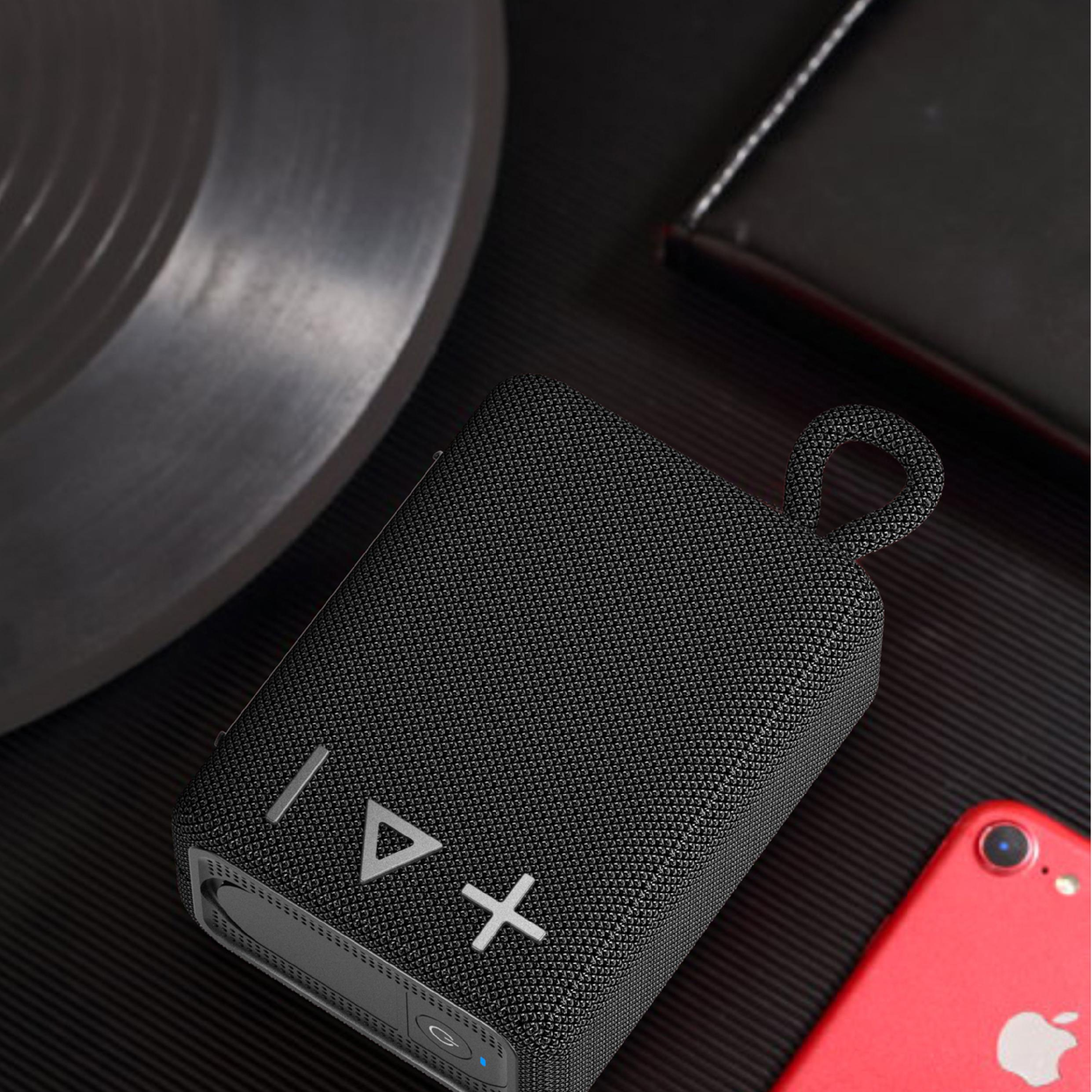 Czarny, przenośny głośnik bluetooth z fakturą materiału, na ciemnej powierzchni obok telefonu.