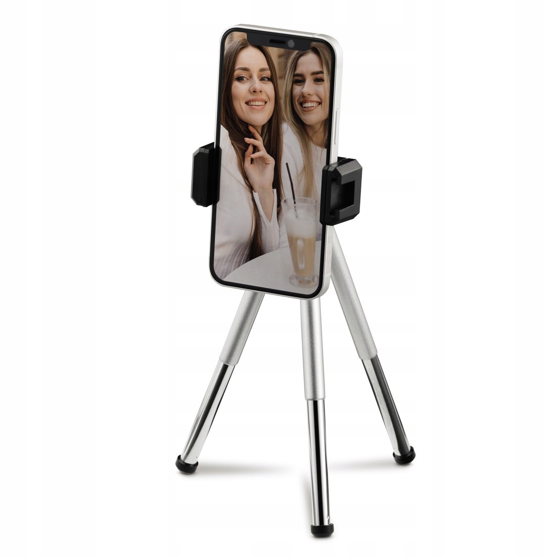 Ein Smartphone mit zwei lächelnden Frauen auf dem Bildschirm steht auf einem silbernen Kleinstativ vor weißem Hintergrund.