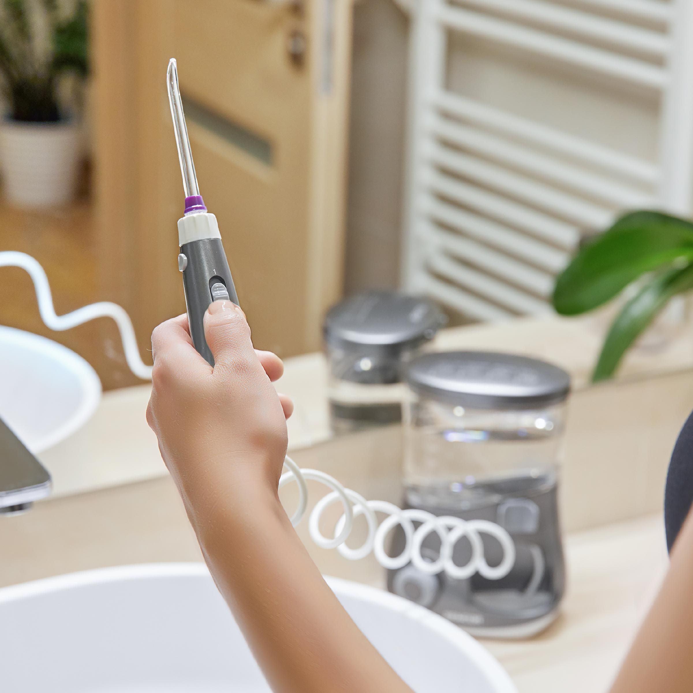 Una mano tiene un manico per idropulsore grigio con un cavo a spirale bianco in bagno.