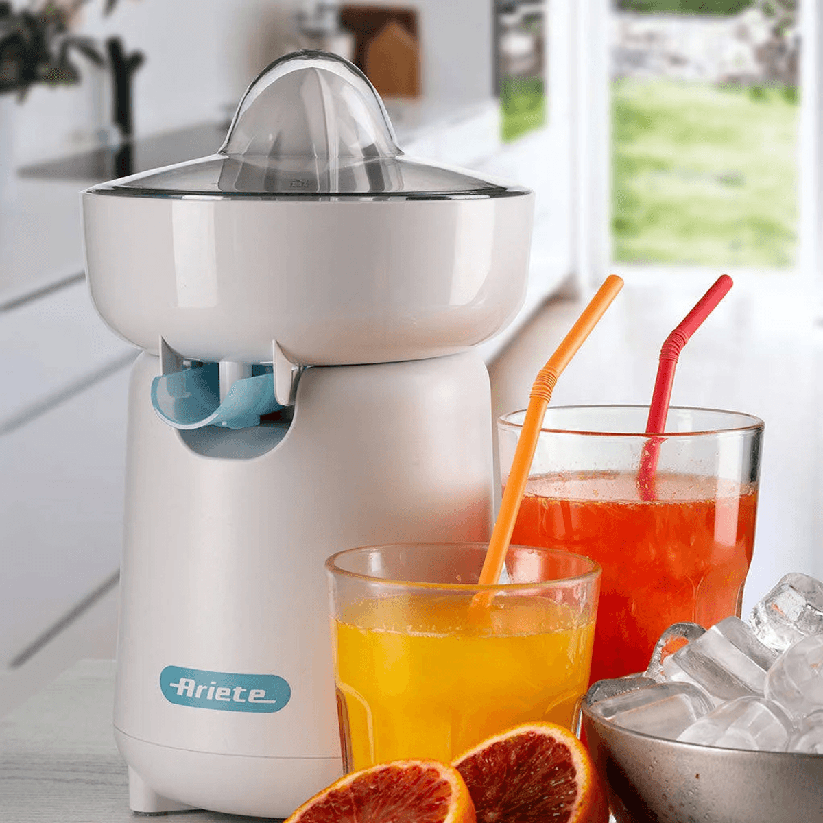 Eine weiße Ariete-Zitruspresse mit Säften, Eiswürfeln und Orangenscheiben auf einem Küchentisch.