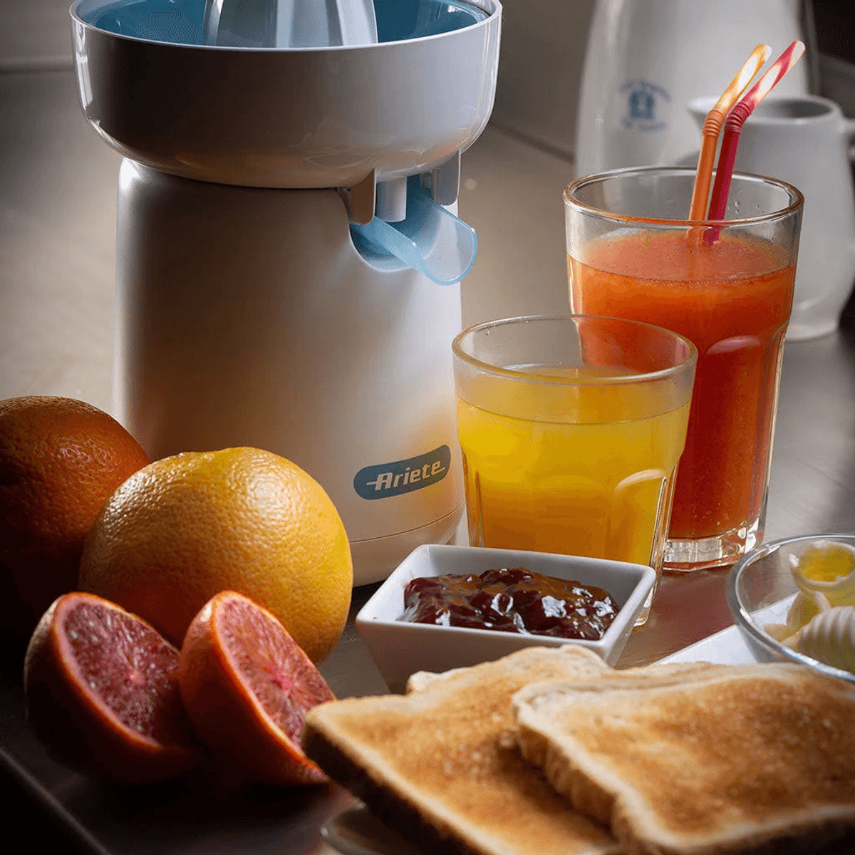 Frühstückstisch mit Zitruspresse, frischen Orangen, Toast, Marmelade und Gläsern mit Saft.