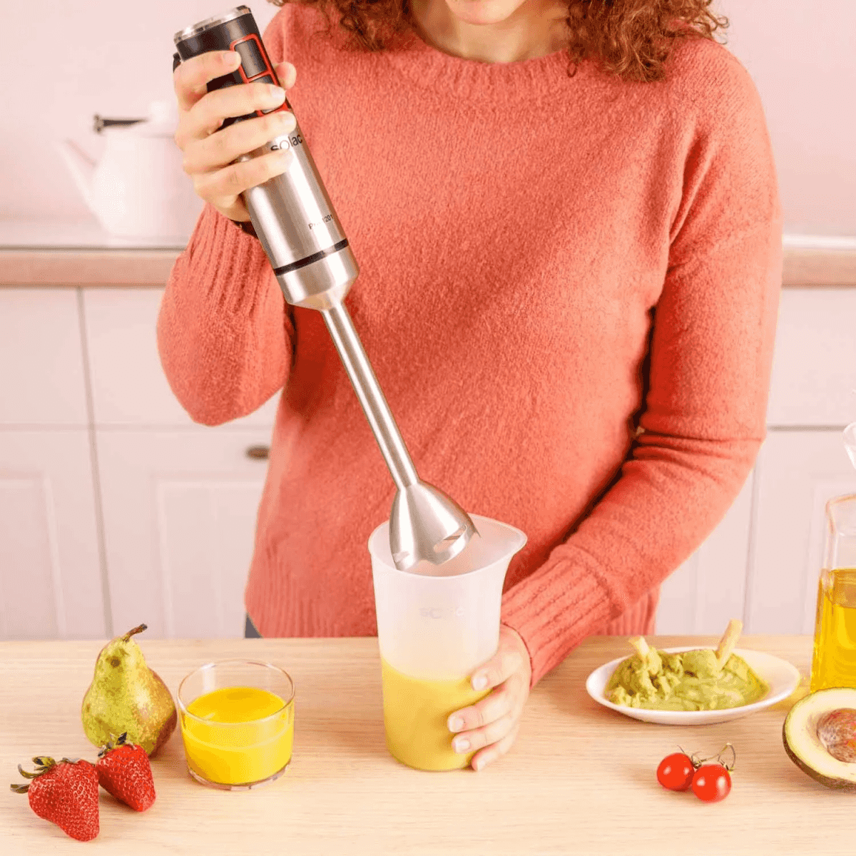 Una mujer con jersey rojo bate un batido con una batidora de mano en una cocina.