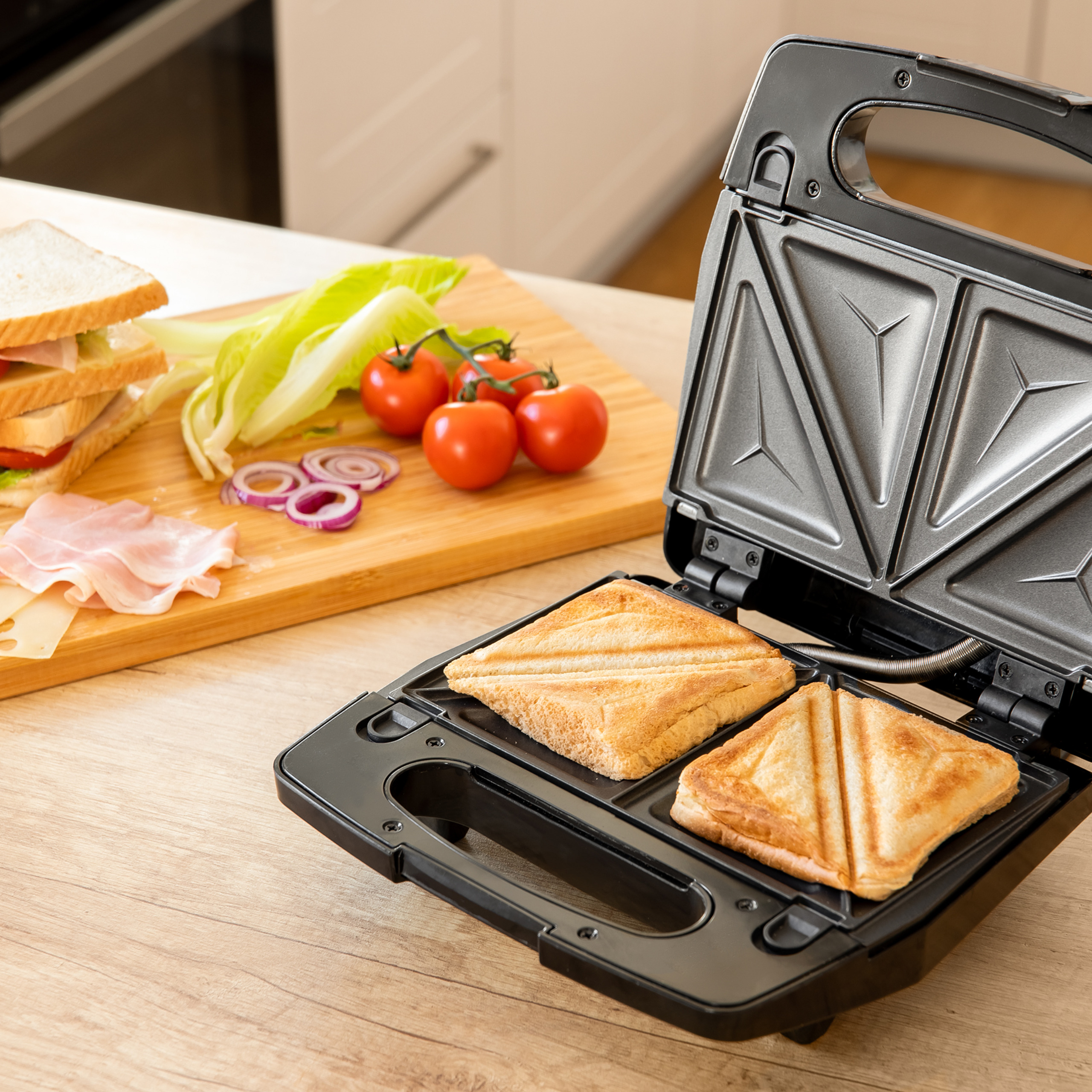 Ein offener Sandwichtoaster mit getoasteten Sandwiches und einem Schneidebrett mit Zutaten im Hintergrund.