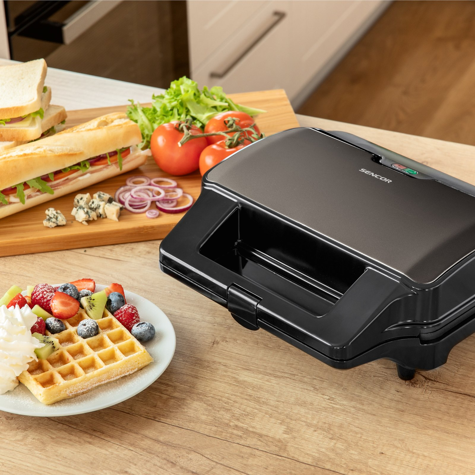 Ein schwarzer Sencor Sandwichtoaster steht auf einer Holztheke neben Waffeln mit Obst und einem Sandwich-Schneidebrett.
