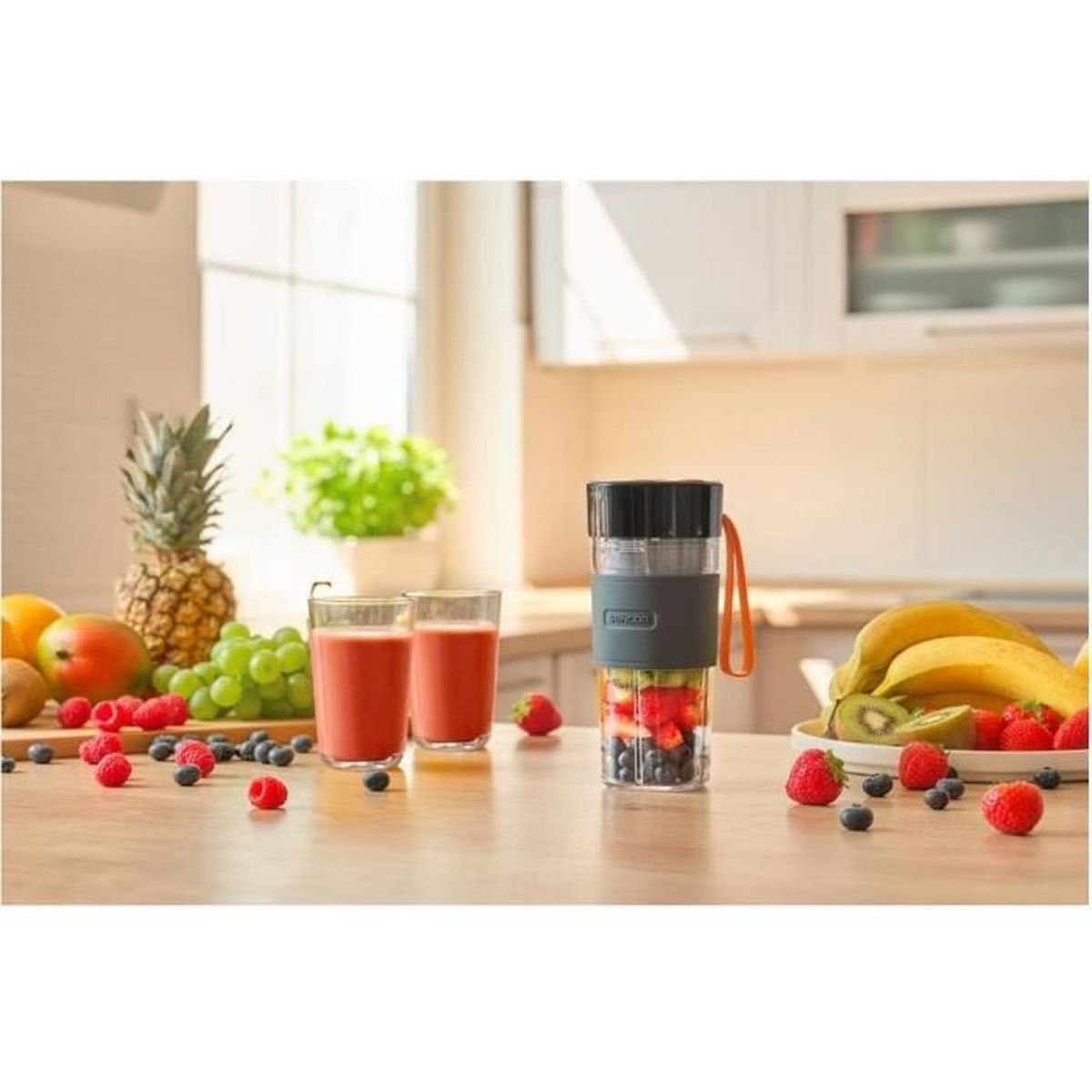 Przenośny blender z owocami i koktajlami na drewnianym blacie kuchennym ze świeżymi owocami.