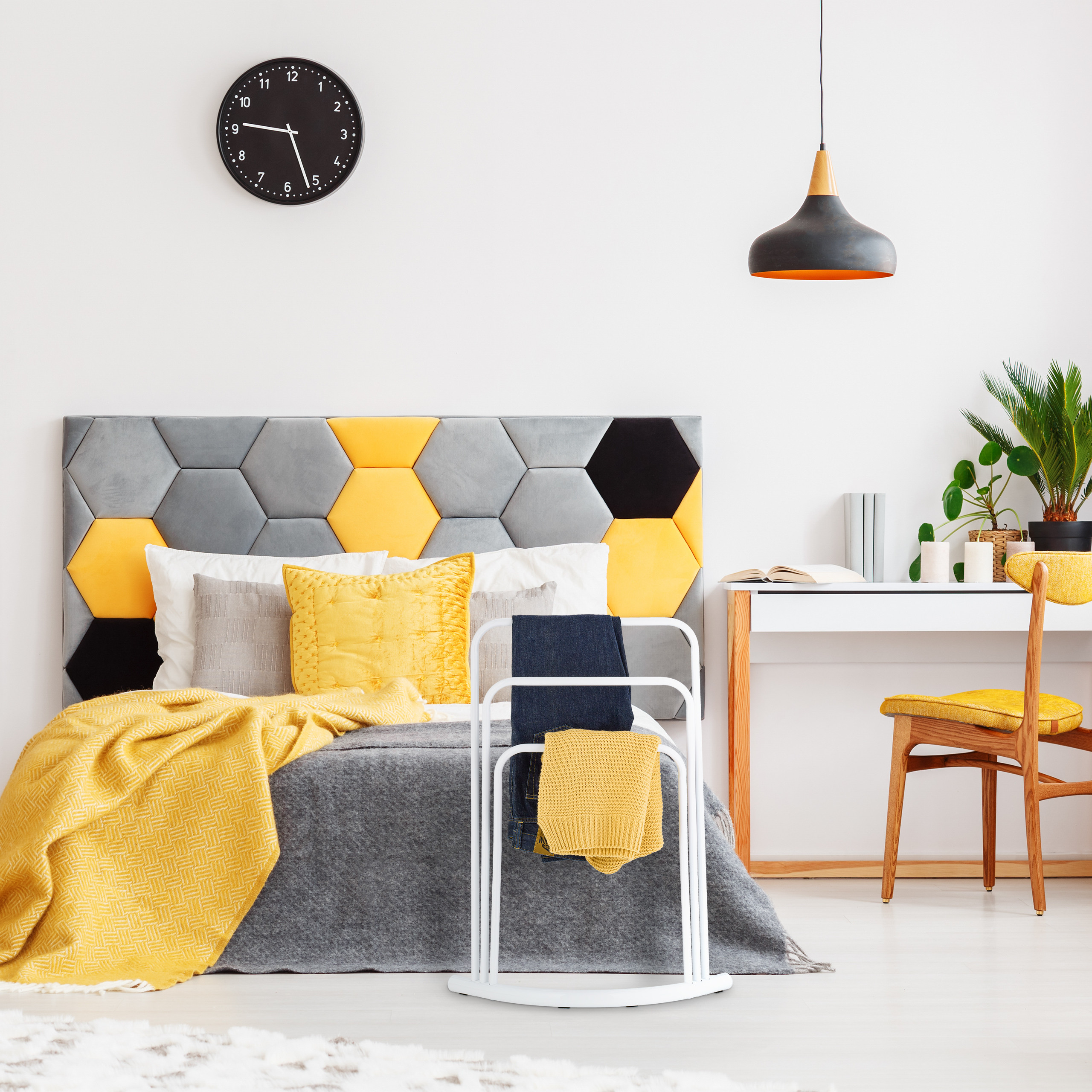 Ein modernes Schlafzimmer mit grau-gelbem Hexagon-Kopfteil, weißem Schreibtisch, Stuhl und Uhr an der Wand.