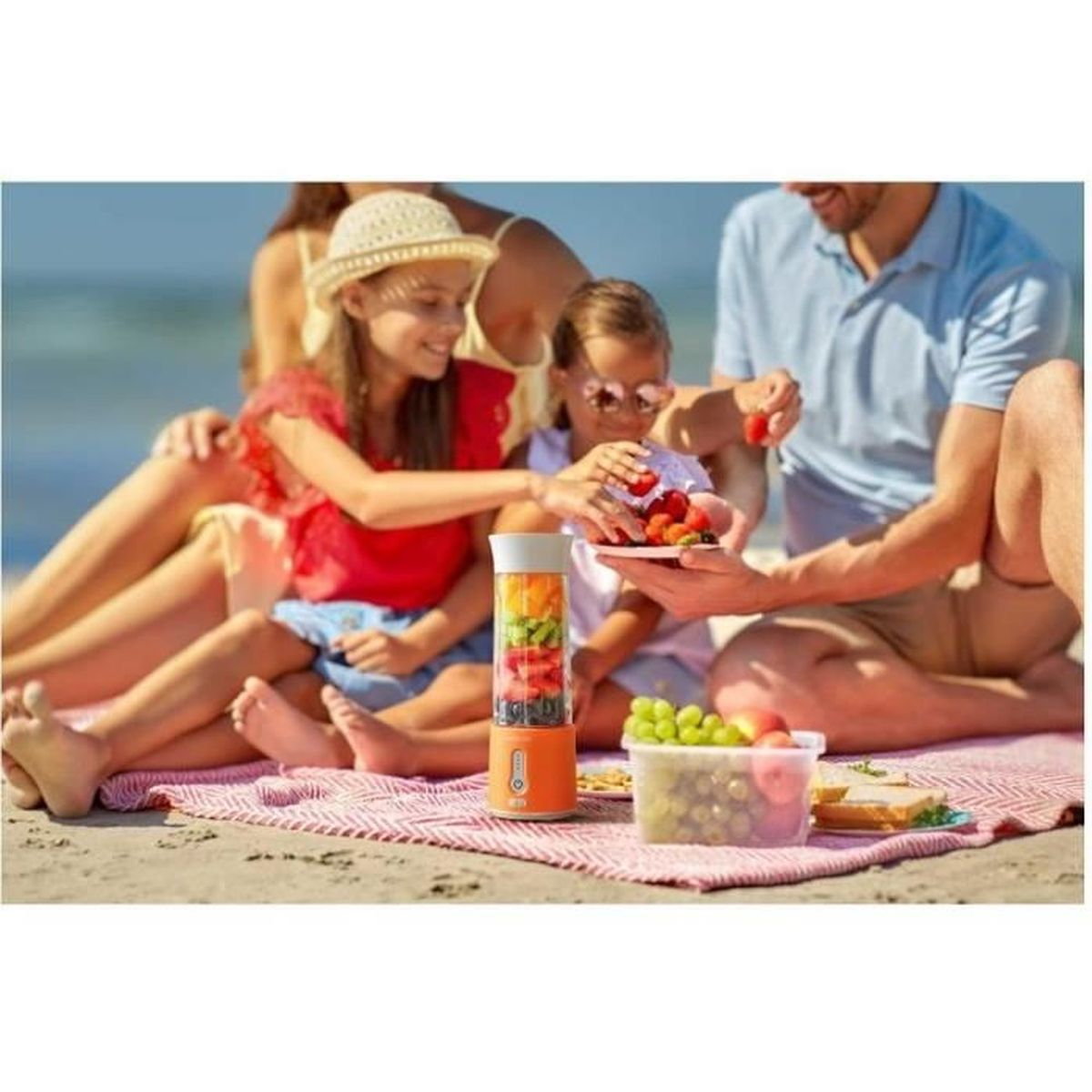 Rodzina ma piknik na plaży, przygotowując owoce w blenderze.