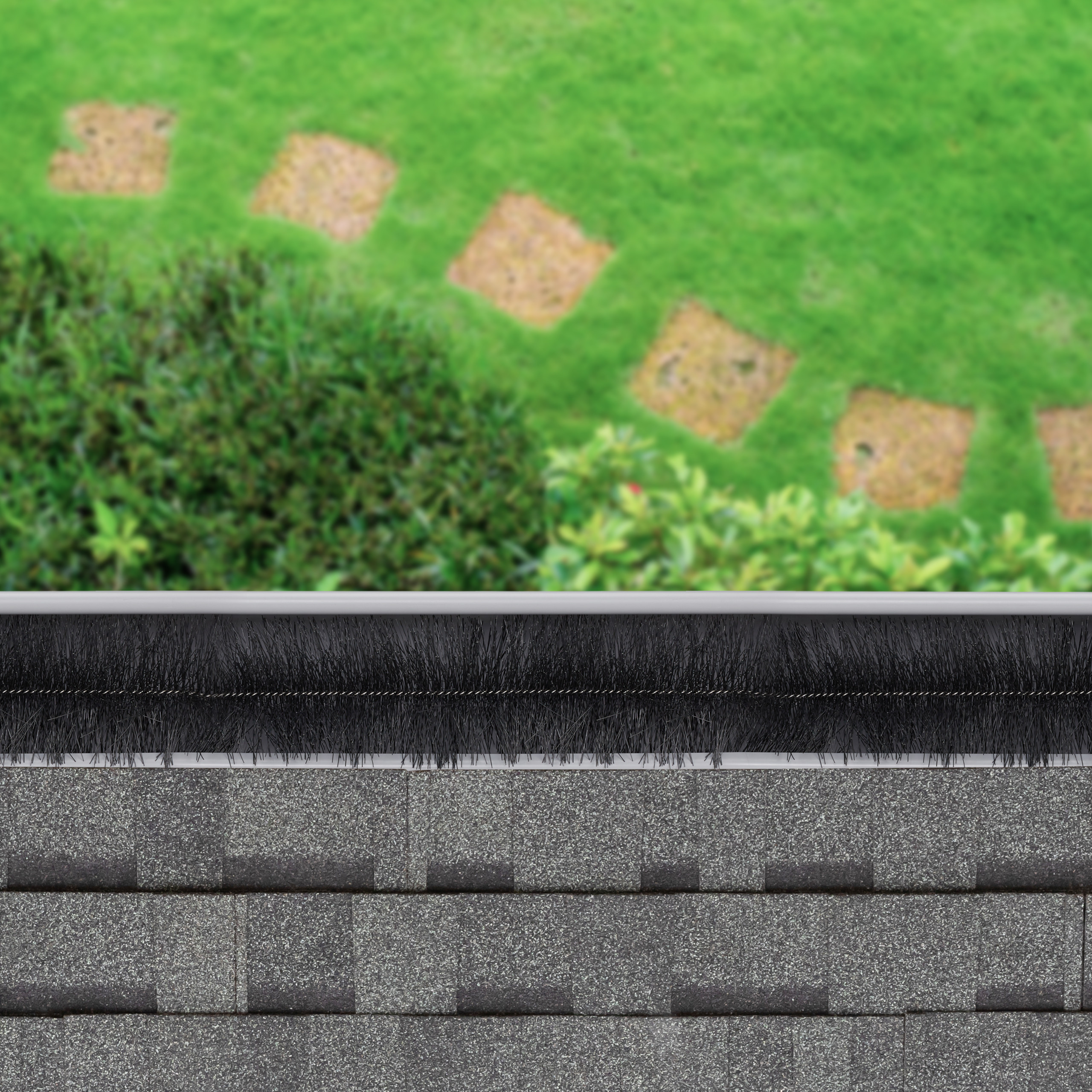 Eine schwarze Dachrinnenbürste in einer Dachrinne, mit Schindeldach und grünem Garten im Hintergrund.
