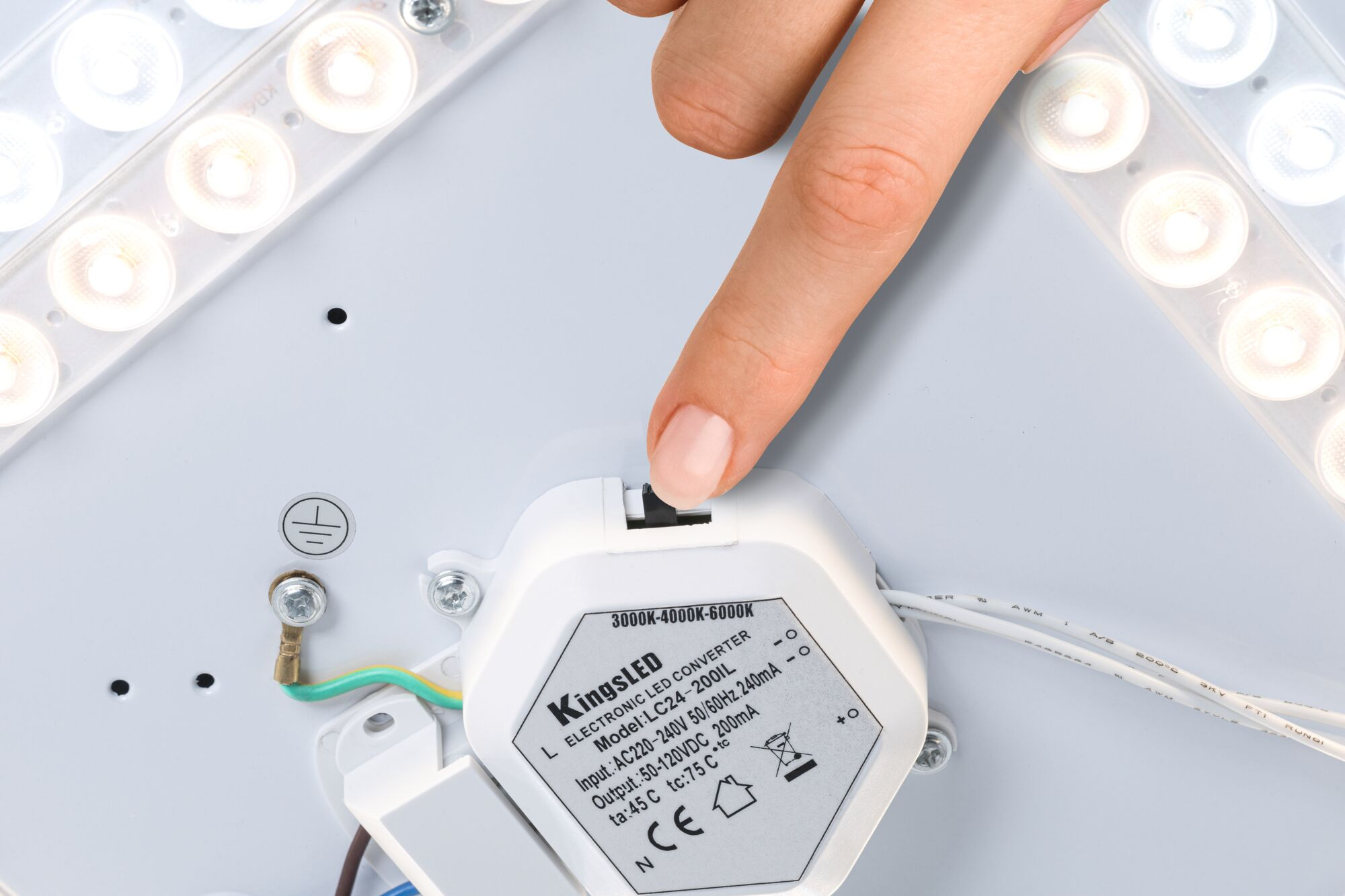 Ein Finger drückt den Schalter eines weißen KingsLED LED-Treibers auf einer Leuchtenmontageplatte.