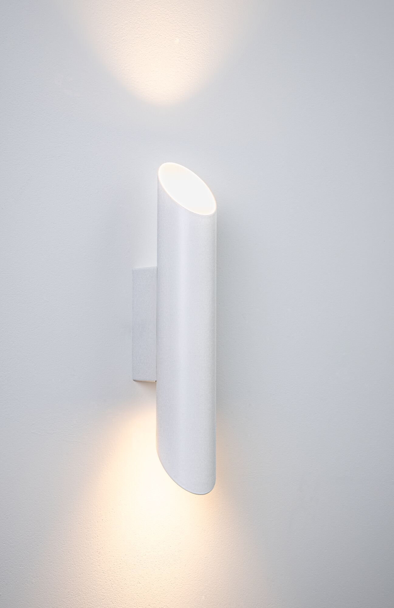 Eine weiße zylindrische Wandleuchte leuchtet nach oben und unten an einer Wand.