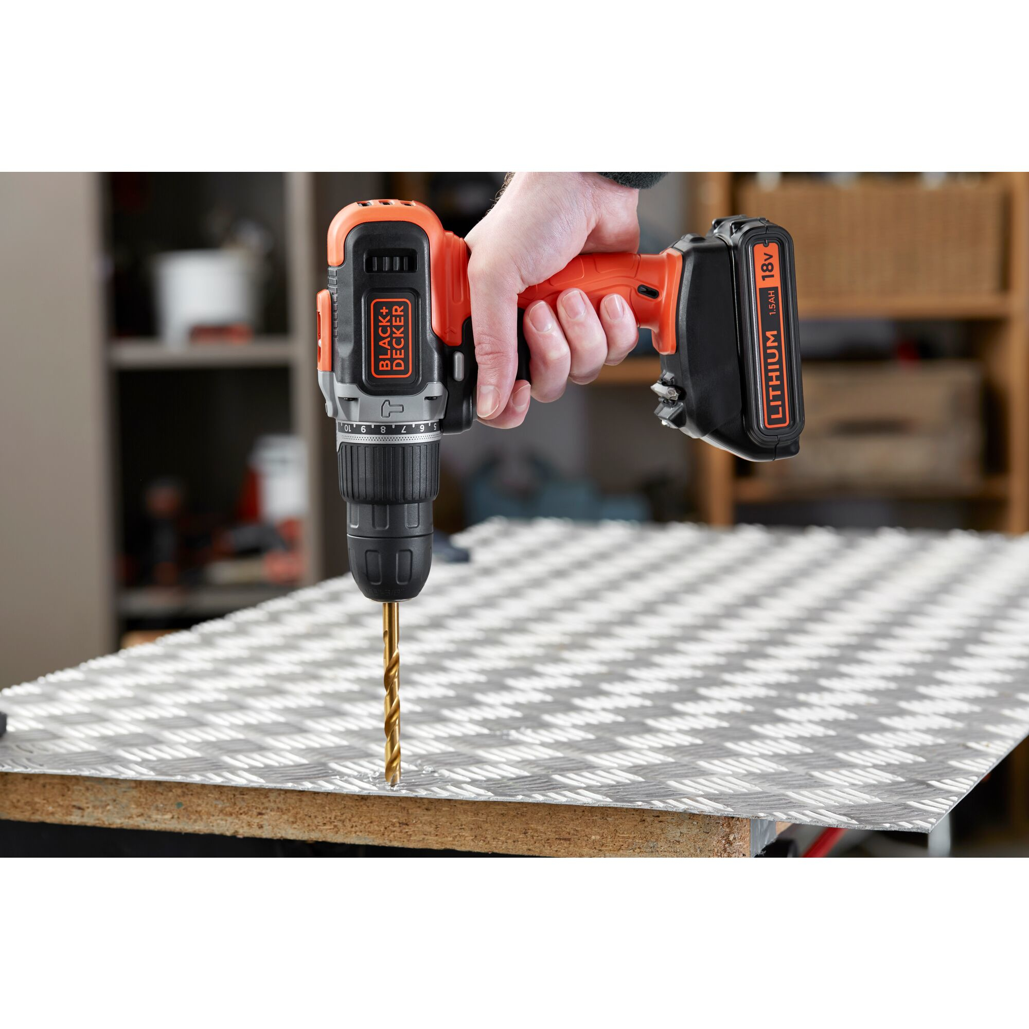 Eine Hand hält eine orange-schwarze Akku-Bohrmaschine, die in ein geriffeltes Metallblech bohrt.