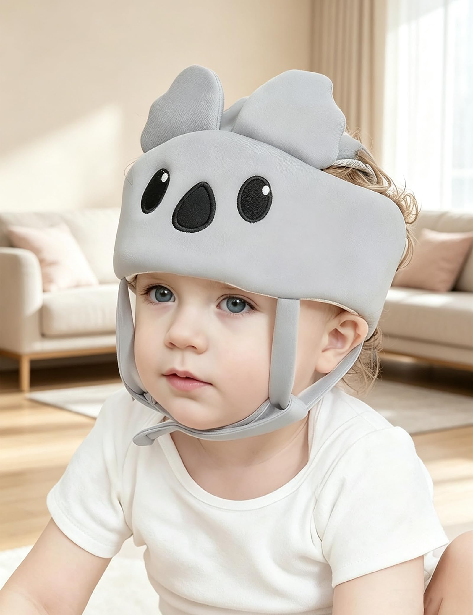 Kleinkind trägt einen grauen Schutzhelm mit Koala-Ohren in einem hellen Wohnzimmer.