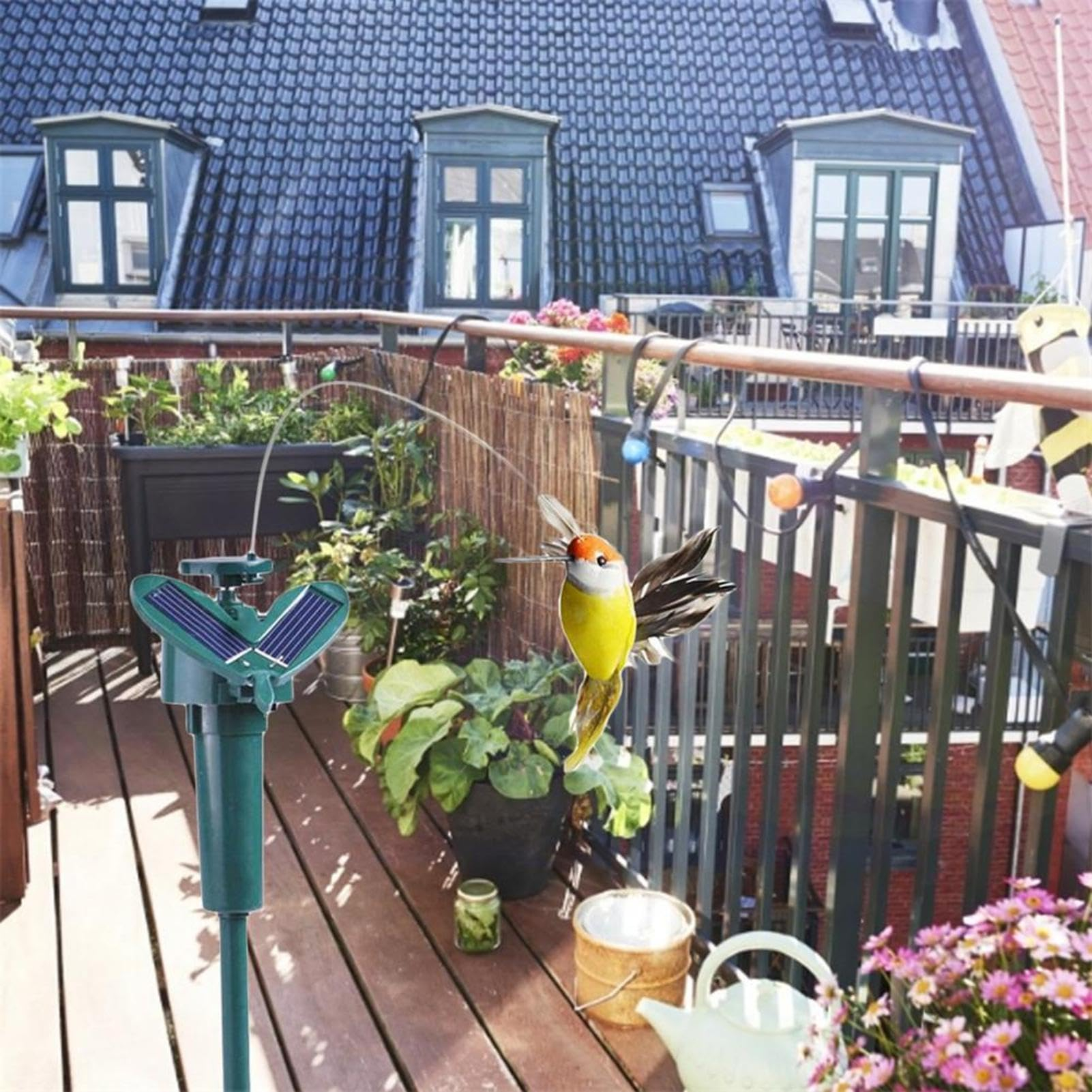 Solarbetriebenes Kolibri-Spielzeug auf einem sonnigen Balkon mit Pflanzen.