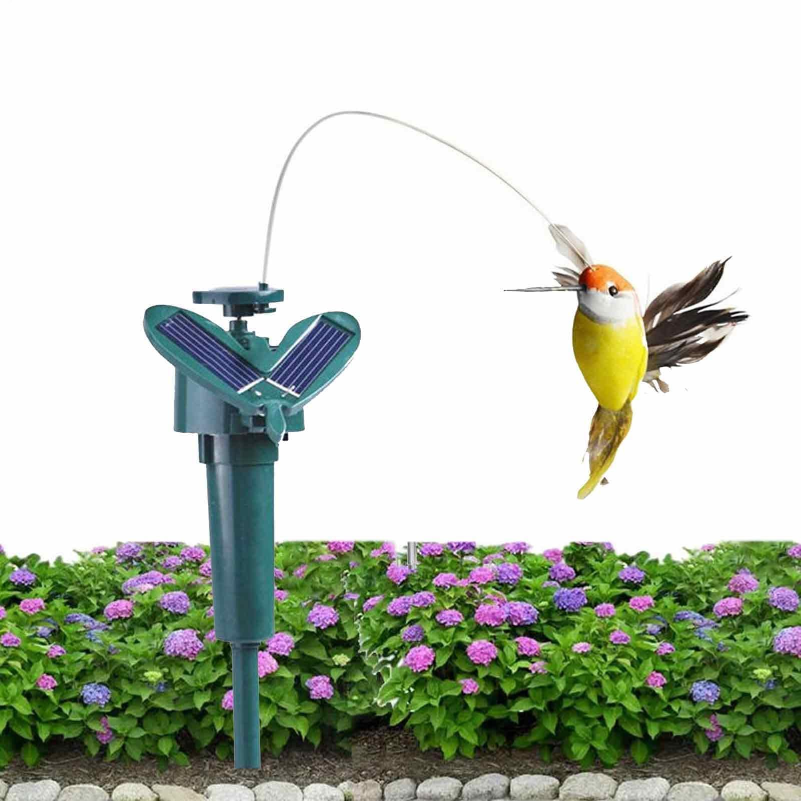Solarbetriebener Kolibri-Stab vor einem grünen Busch mit lila Blumen auf weißem Hintergrund.