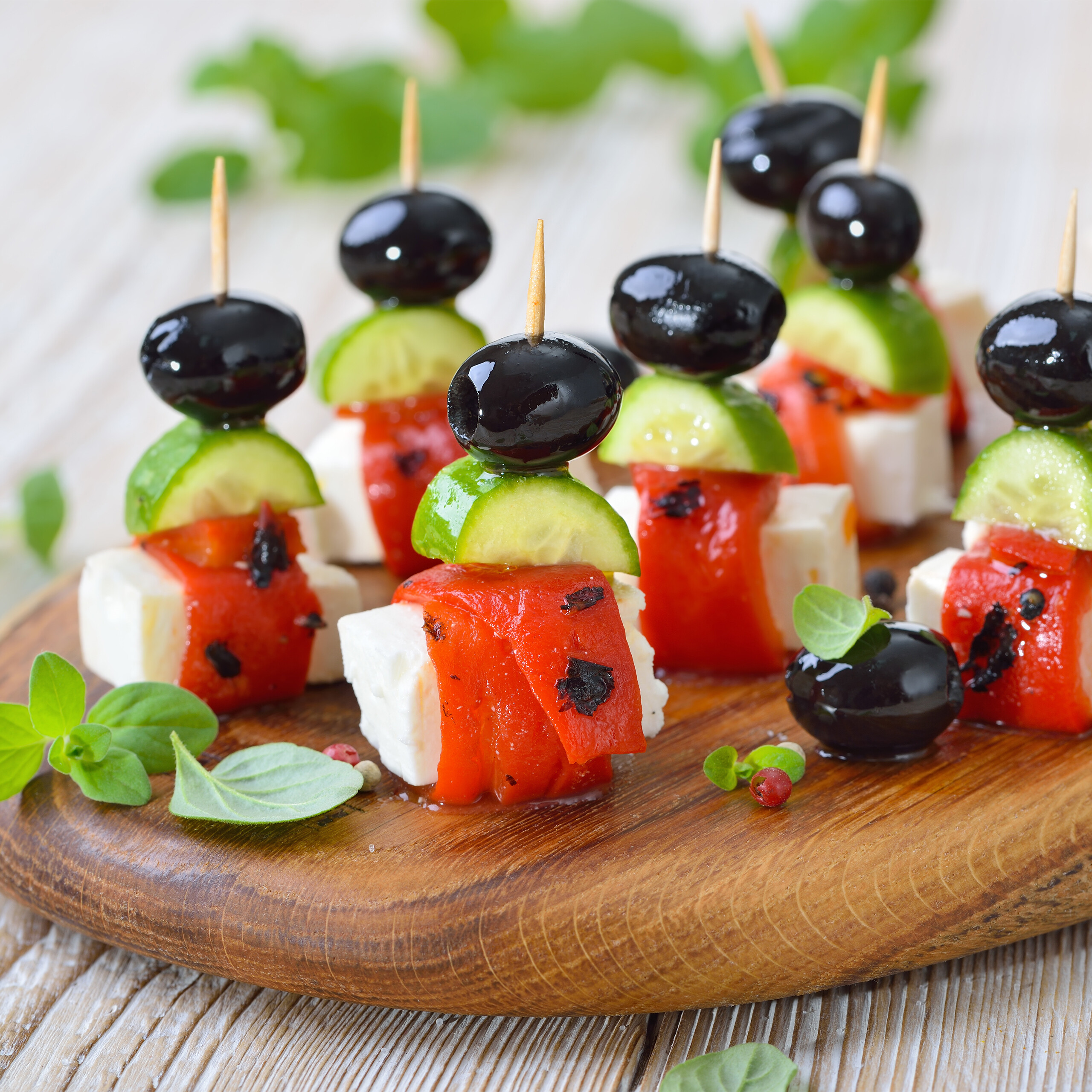 Griechische Salat-Spieße mit Feta, roter Paprika, Gurke und Olive auf Holzbrett.