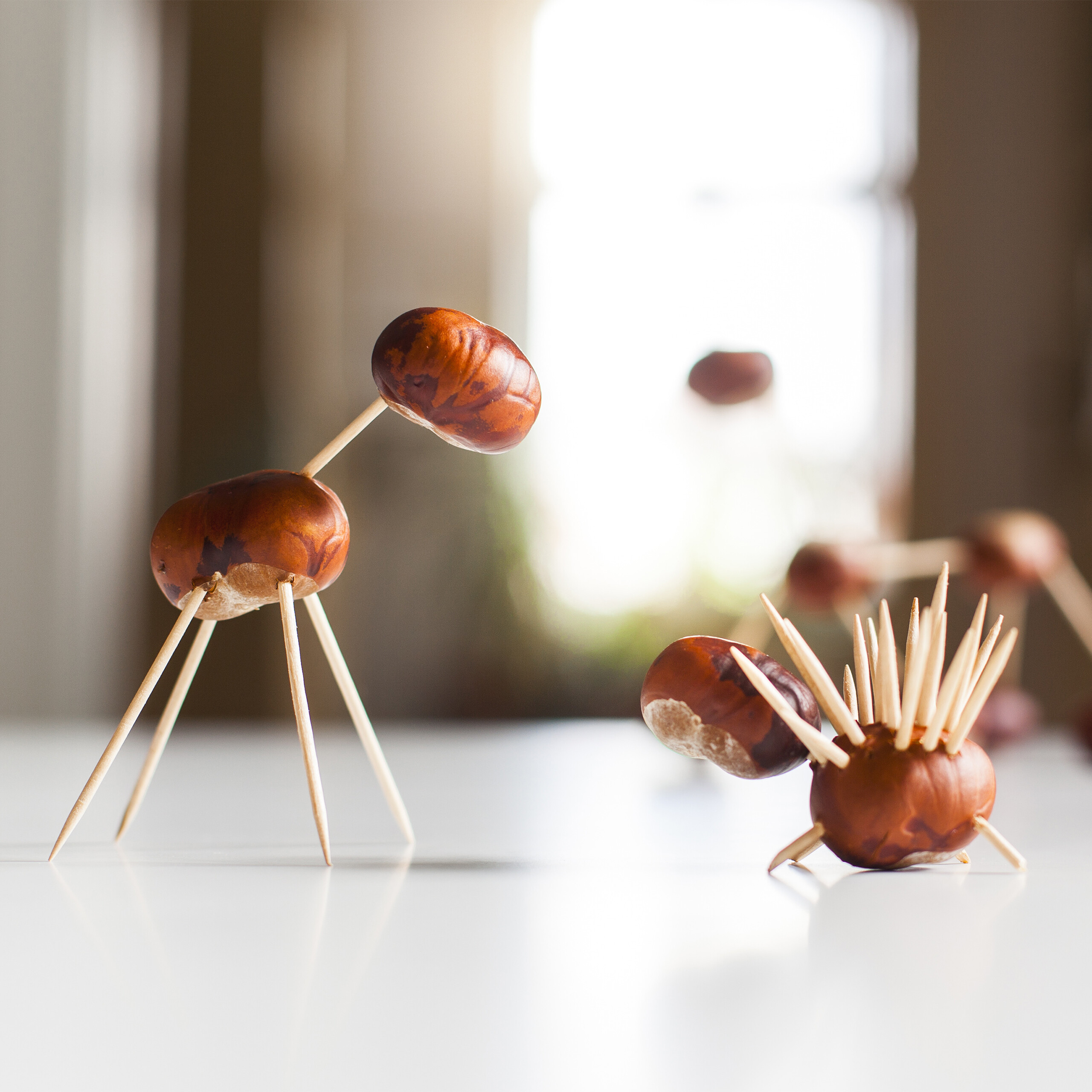 Handgemachte Kastanienfiguren, eine giraffe-ähnliche und eine igel-ähnliche, stehen auf einem Tisch.