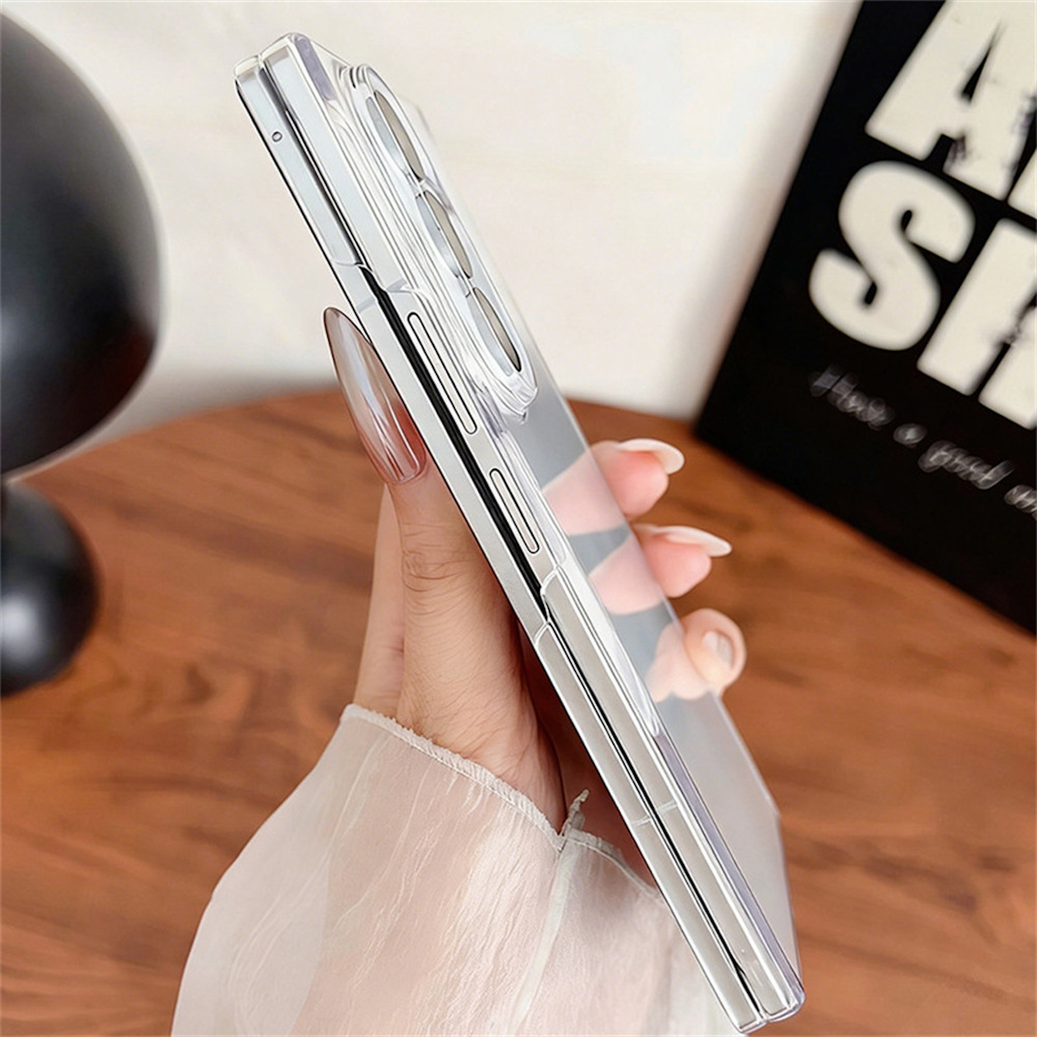 Eine Hand hält ein gefaltetes Smartphone in einer klaren Schutzhülle auf einem Holztisch.