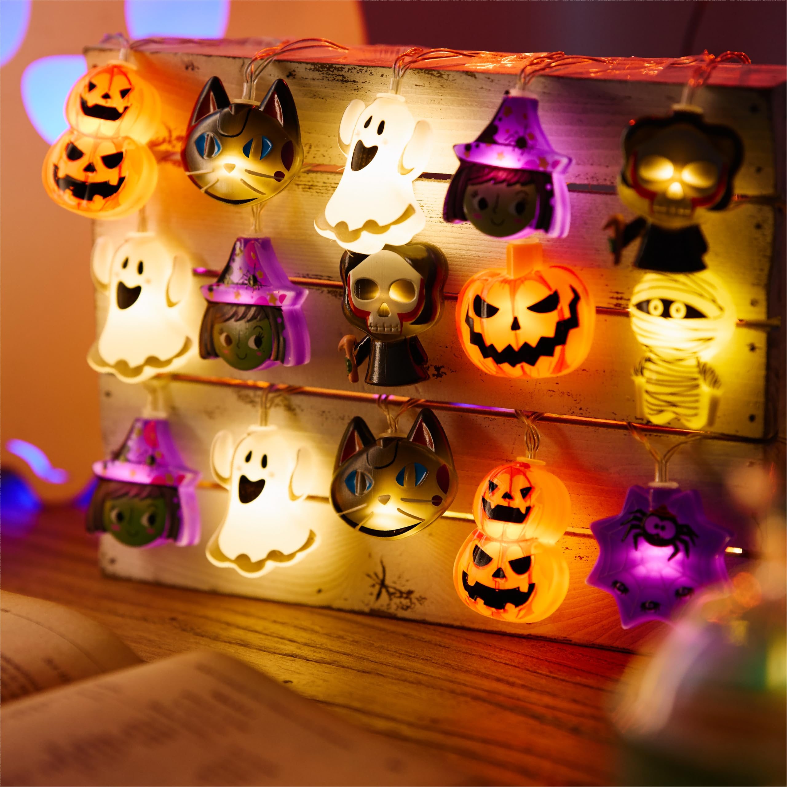 Bunte Halloween-Lichterkette mit Kürbissen, Geistern und Hexen auf Holz.