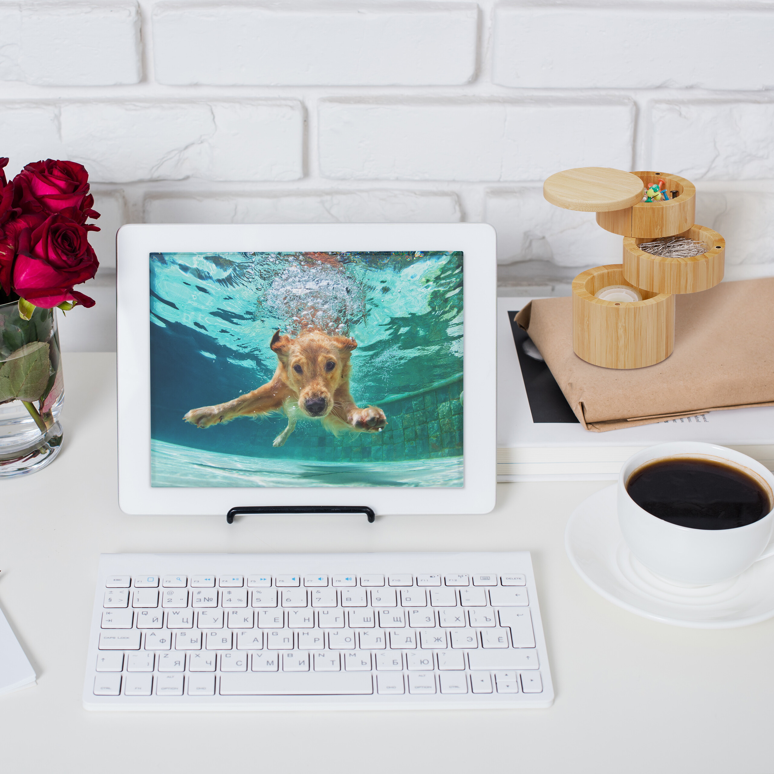 Ein Tablet zeigt einen schwimmenden Hund, daneben liegen Blumen, eine Tastatur, eine Kaffeetasse und eine Holzbox.