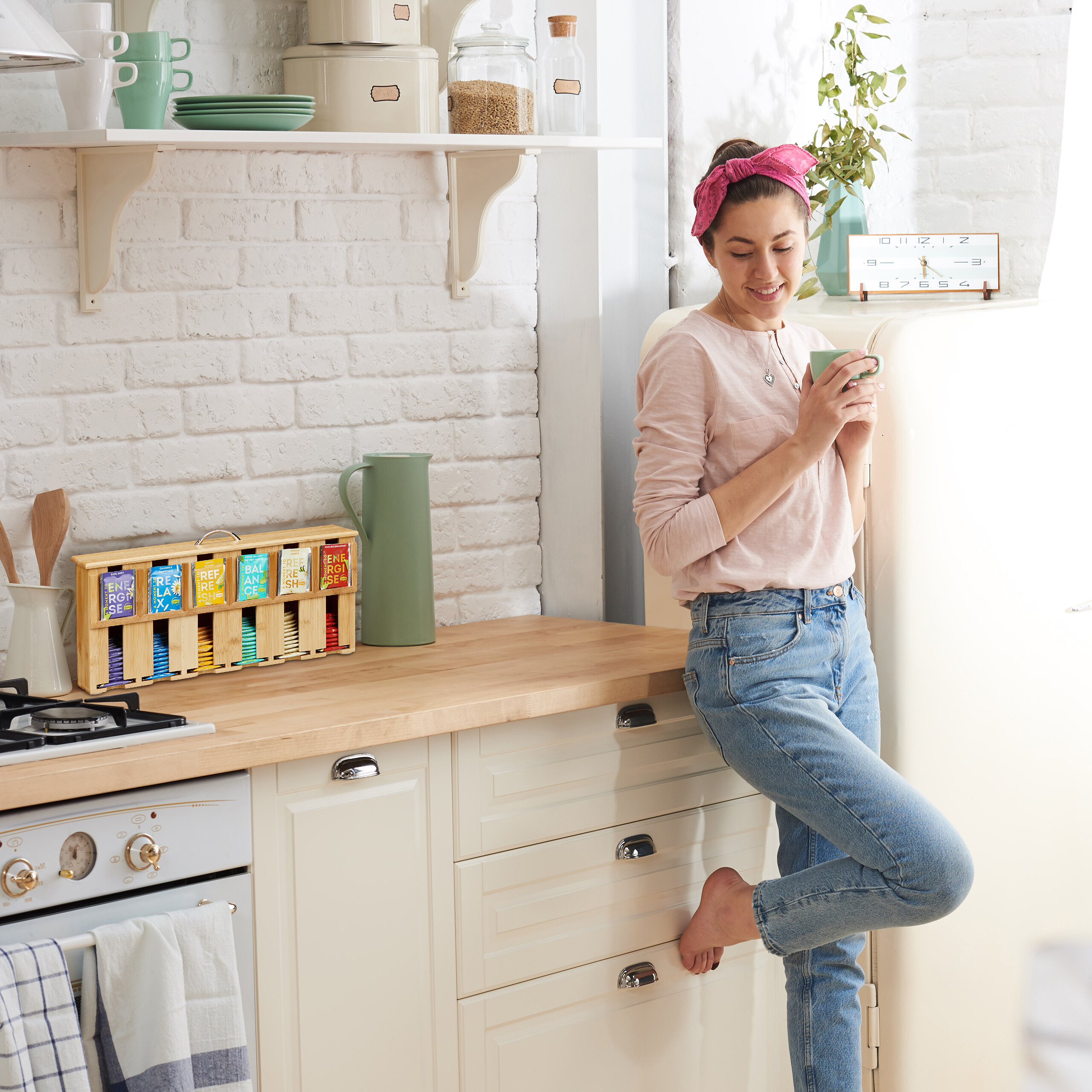 Eine Frau in rosa Shirt und Jeans steht in einer hellen Küche und trinkt aus einer grünen Tasse.