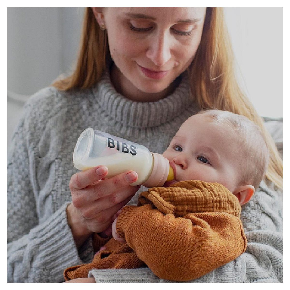 Eine Frau in einem grauen Pullover füttert ein Baby mit einer BIBS-Flasche.