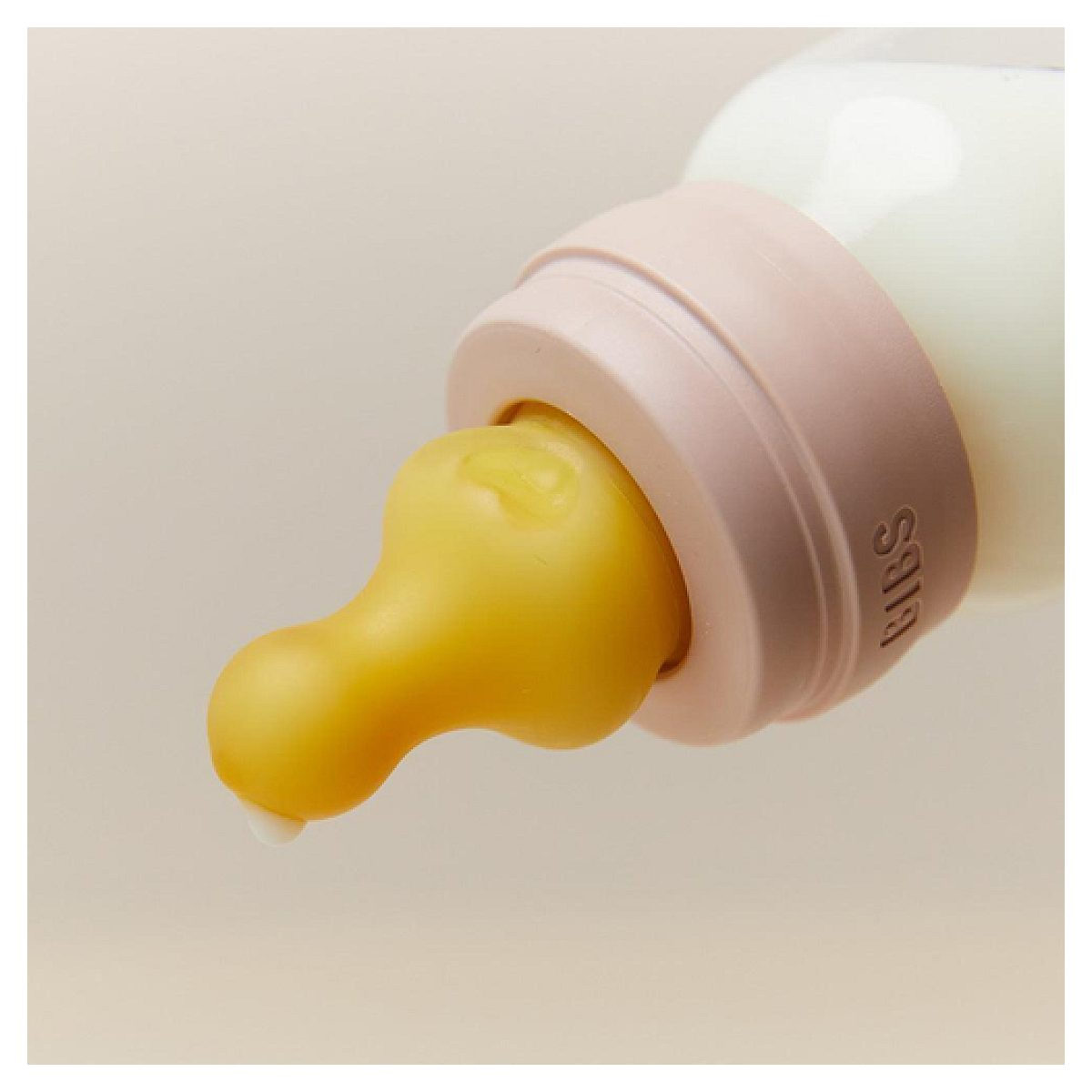 Nahaufnahme einer Babyflasche mit gelbem Sauger und einem Wassertropfen auf hellem Hintergrund.