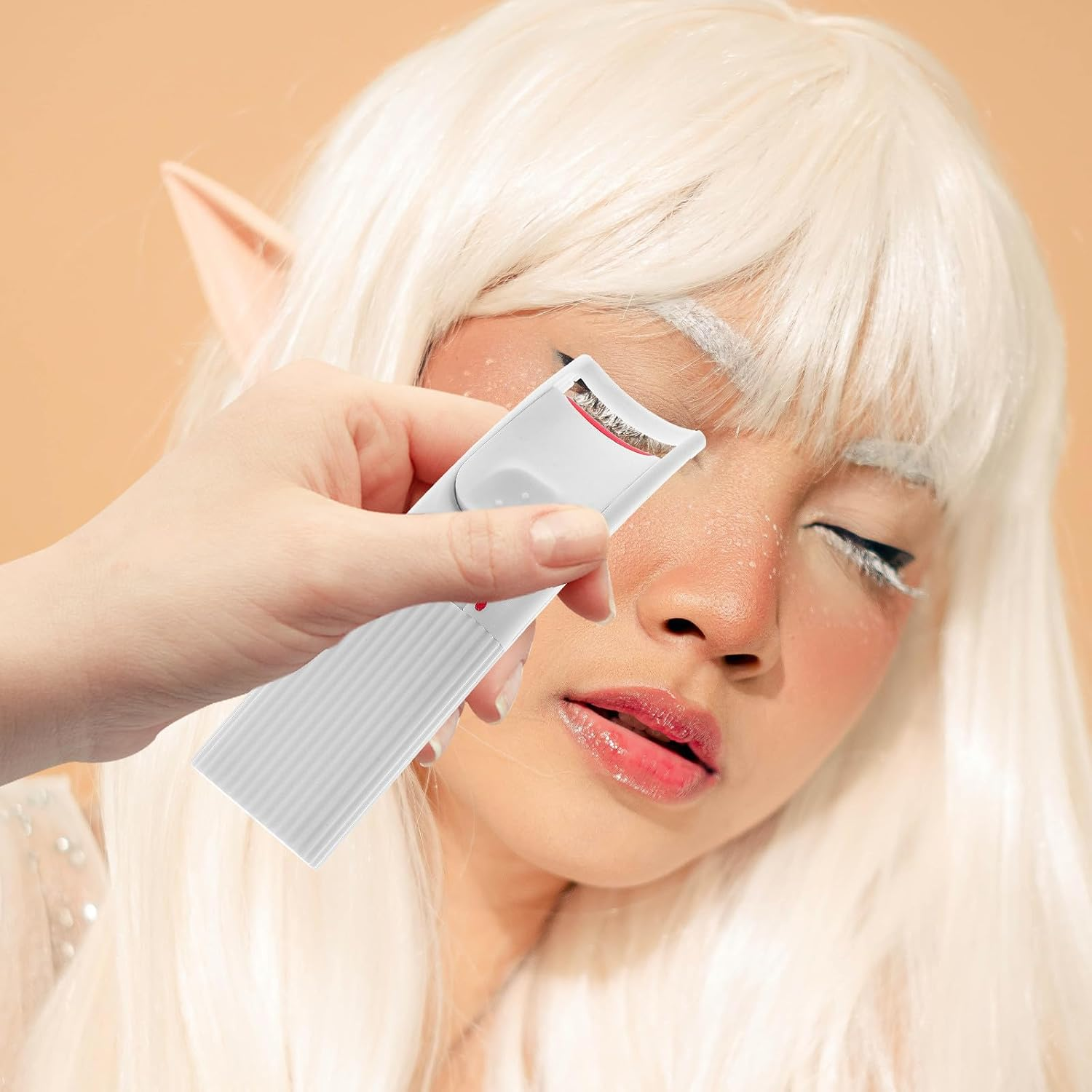 Jemand benutzt eine weiße beheizbare Wimpernzange bei einer Person mit weißer Perücke.