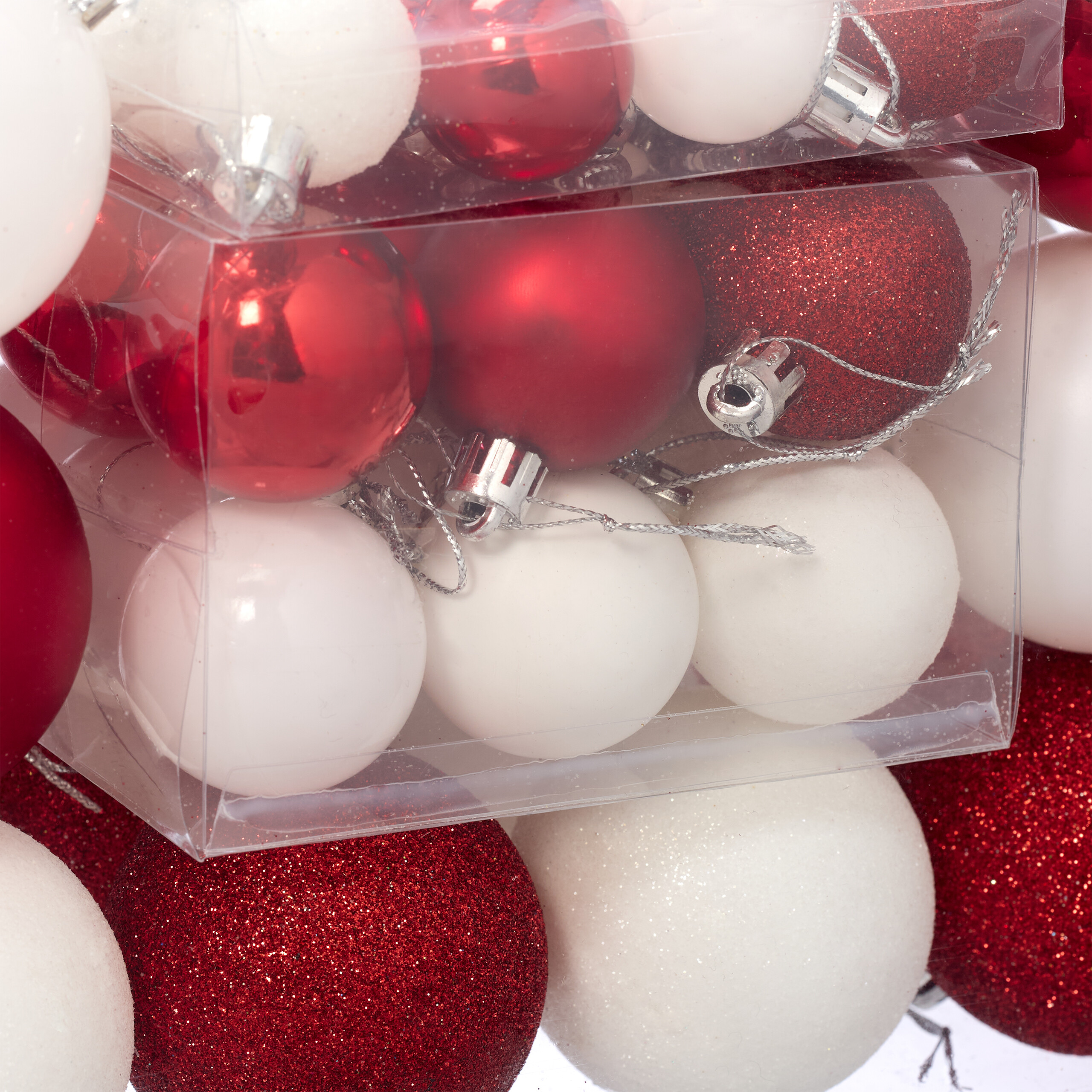 Nahaufnahme von transparenten Boxen mit glänzenden und glitzernden roten und weißen Christbaumkugeln.