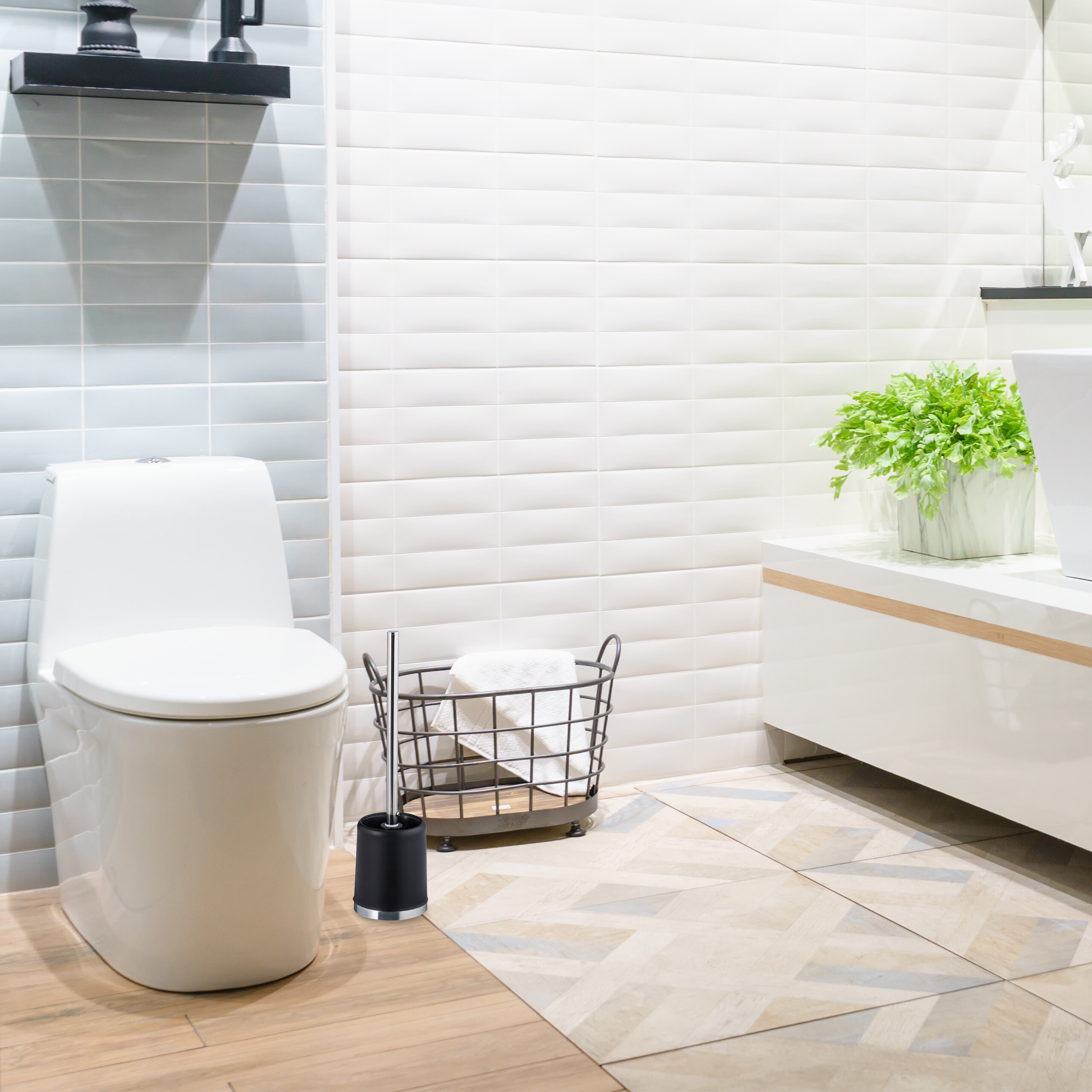 Eine moderne weiße Toilette, eine schwarze Klobürste, ein Drahtkorb mit Handtuch und eine grüne Pflanze in einem weißen Bad.