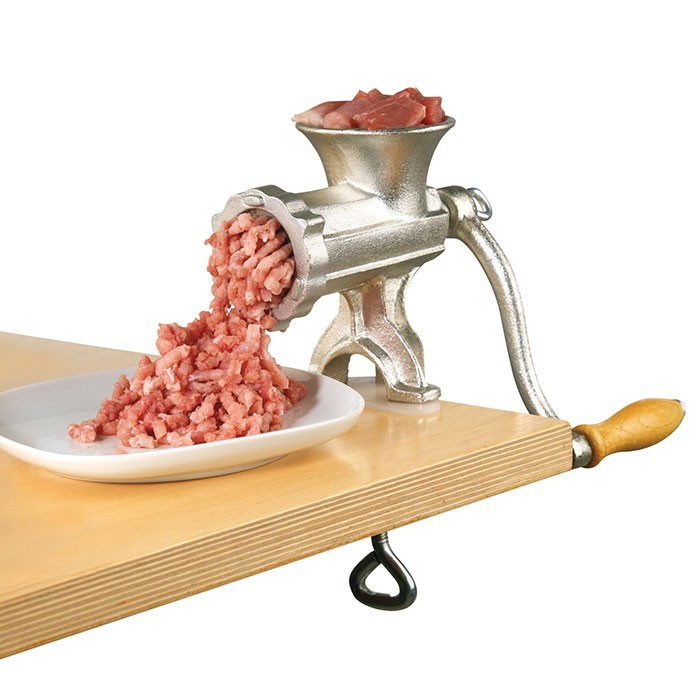 Ein silberner Fleischwolf auf einem Holztisch mahlt Fleisch in einen weißen Teller.