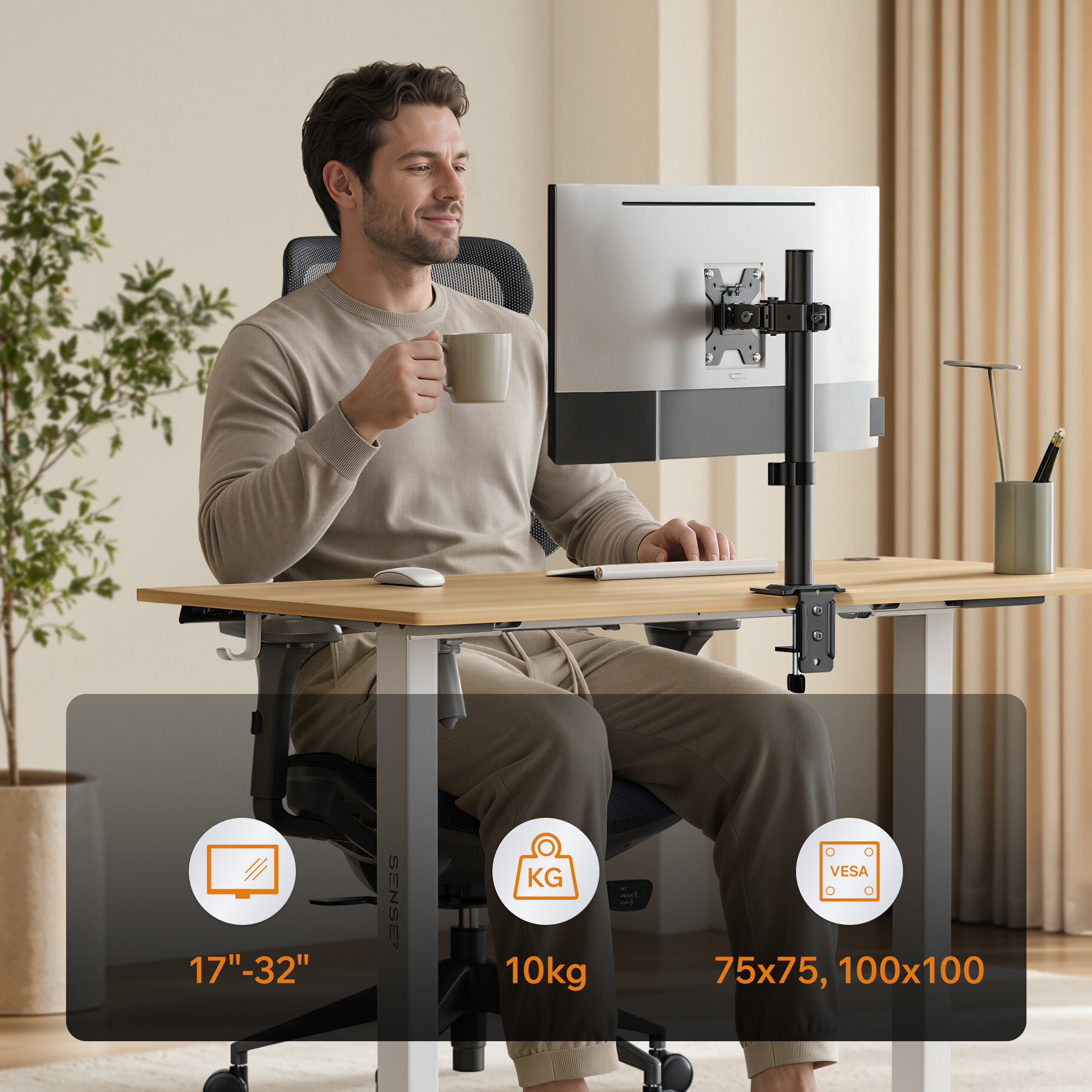 Ein Mann sitzt an einem höhenverstellbaren Holztisch, hält eine Tasse und schaut auf einen montierten Monitor.