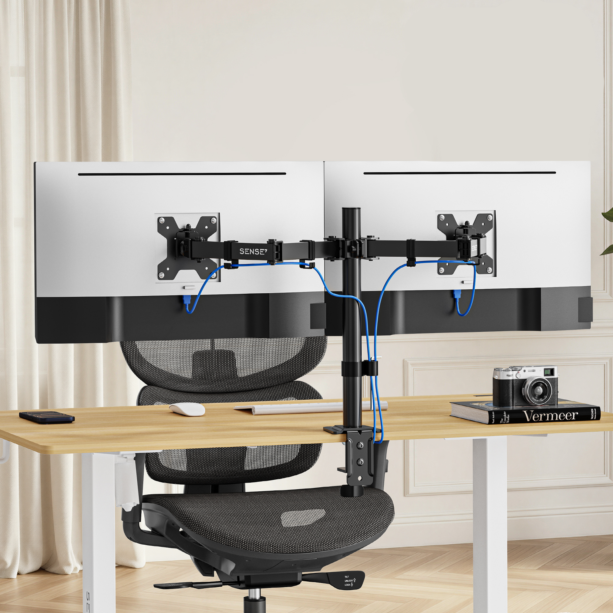 Zwei Monitore auf einem Tisch mit Ständer, schwarzer Stuhl und Kamera.