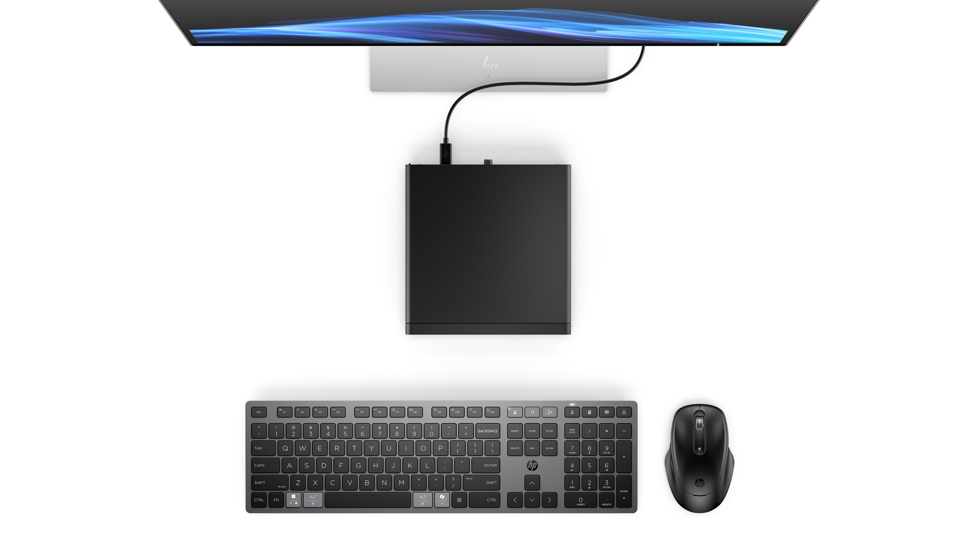 Widok z góry na biurko z monitorem, mini komputerem, klawiaturą i myszą na białym tle.