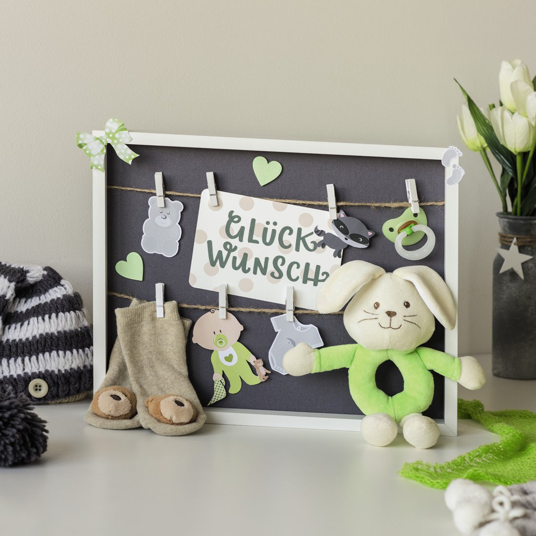 Ein Babysetzbrett mit Kleidung, Spielzeug und dem deutschen Text Glück Wunsch.