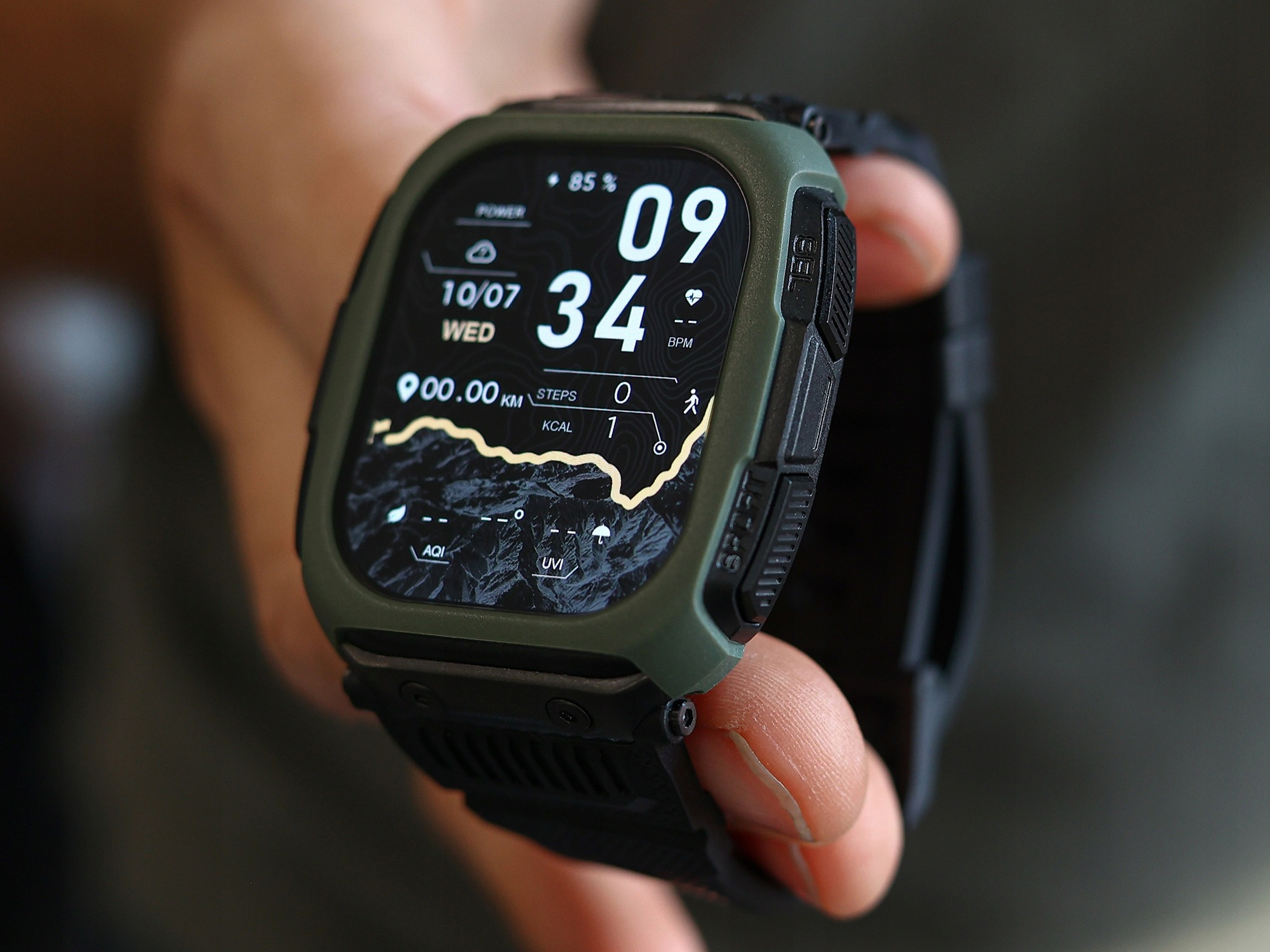 Ręka trzyma zielony smartwatch z czarną kopertą i cyfrową tarczą na ciemnym tle.