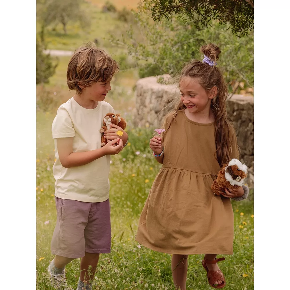 Un niño y una niña sonríen mientras sostienen peluches y flores en un campo.