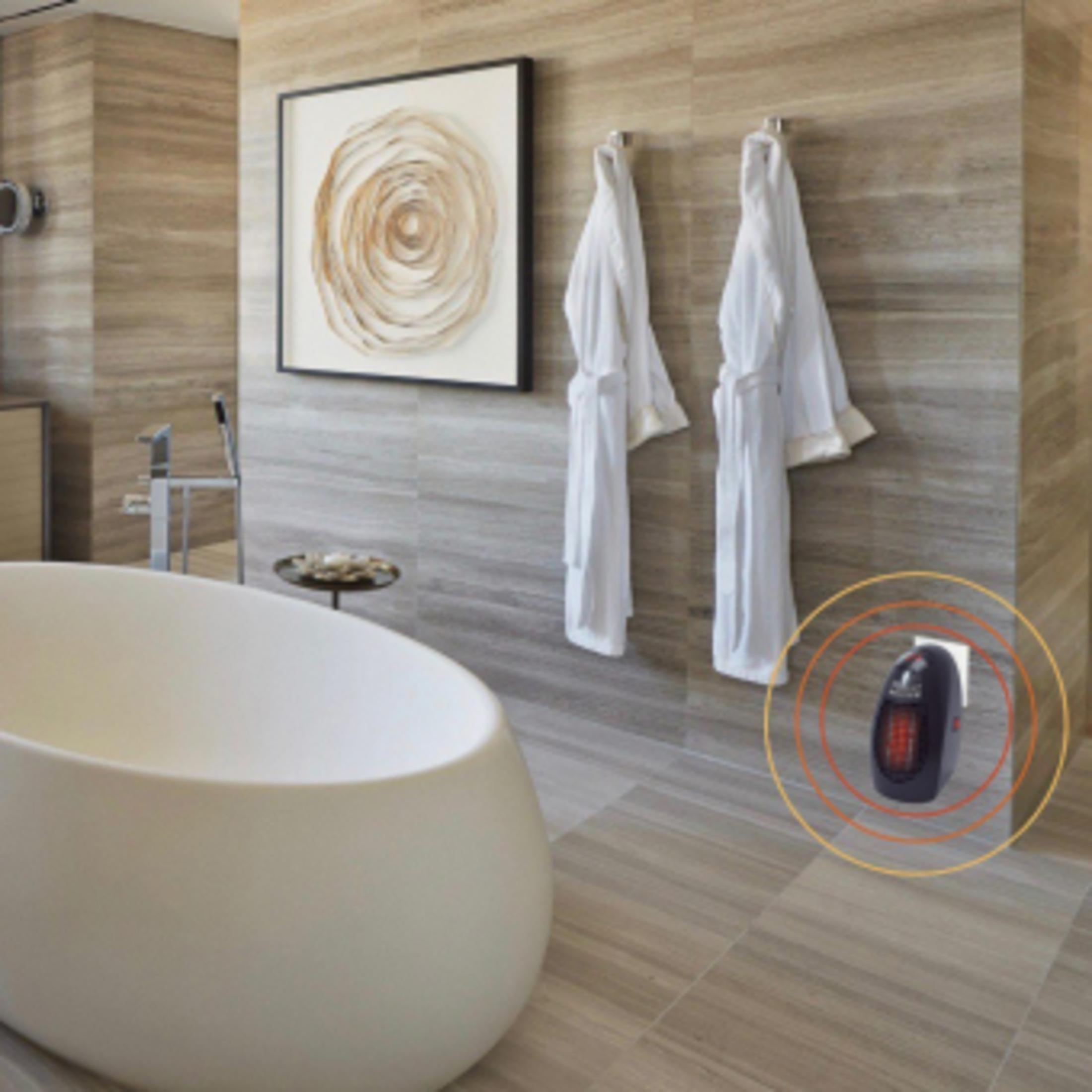 Ein modernes Bad mit weißer Wanne, zwei hängenden Bademänteln und einem kleinen schwarzen Heizgerät in Steckdosennähe.
