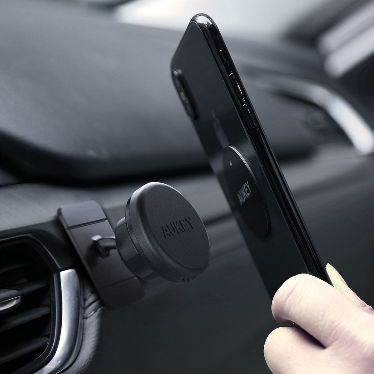 Bir el, AUKEY markalı manyetik araç havalandırma ızgarası tutucusuna siyah bir akıllı telefon takıyor.