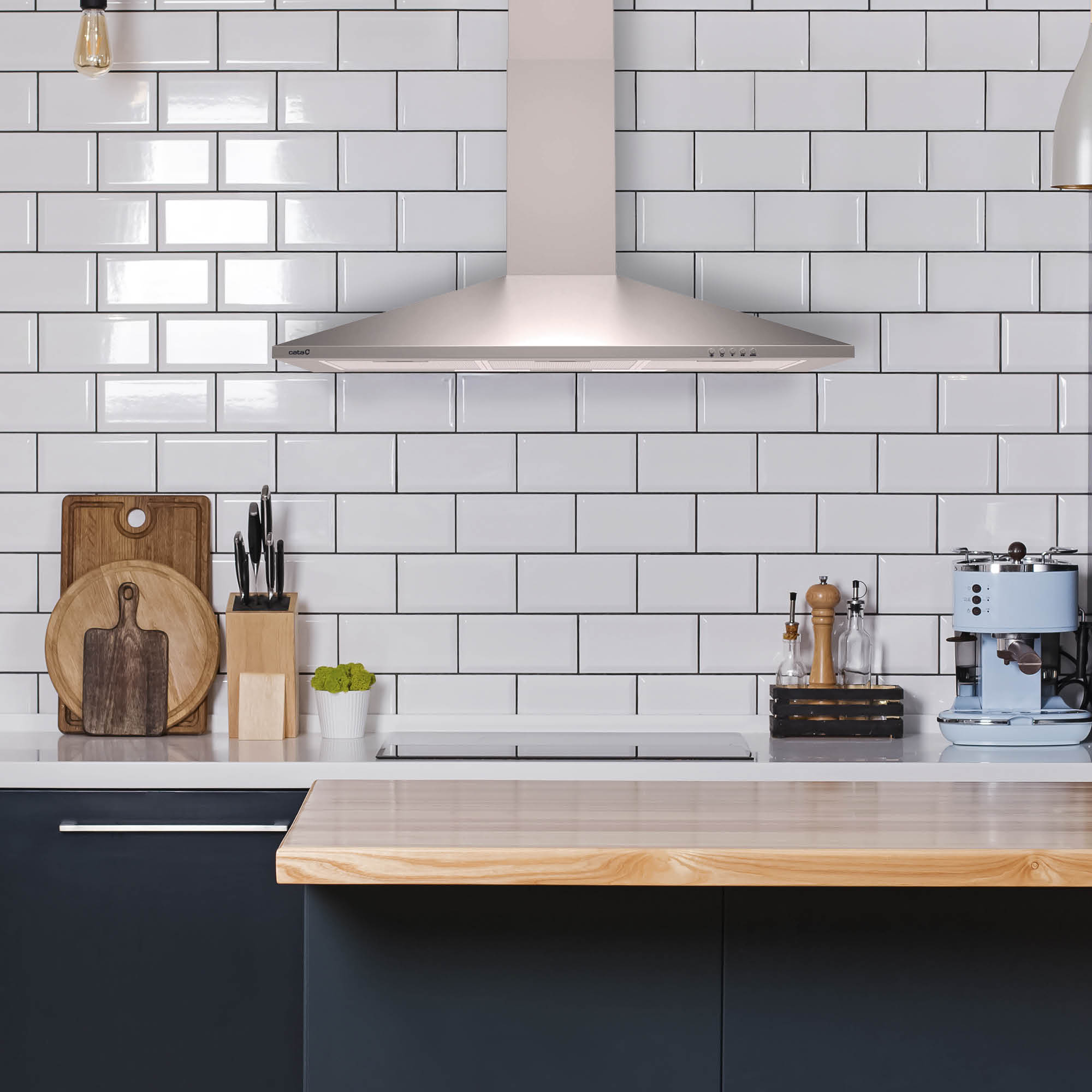 Cocina moderna con azulejos blancos, campana extractora, cafetera, tablas de cortar y utensilios.