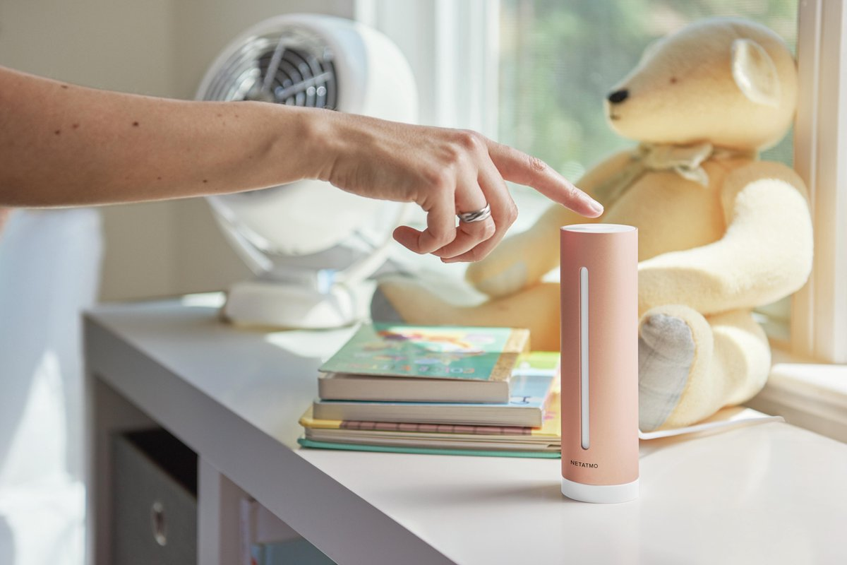 Une main touche un appareil cylindrique rose sur une table à côté de livres et d'un ours en peluche.