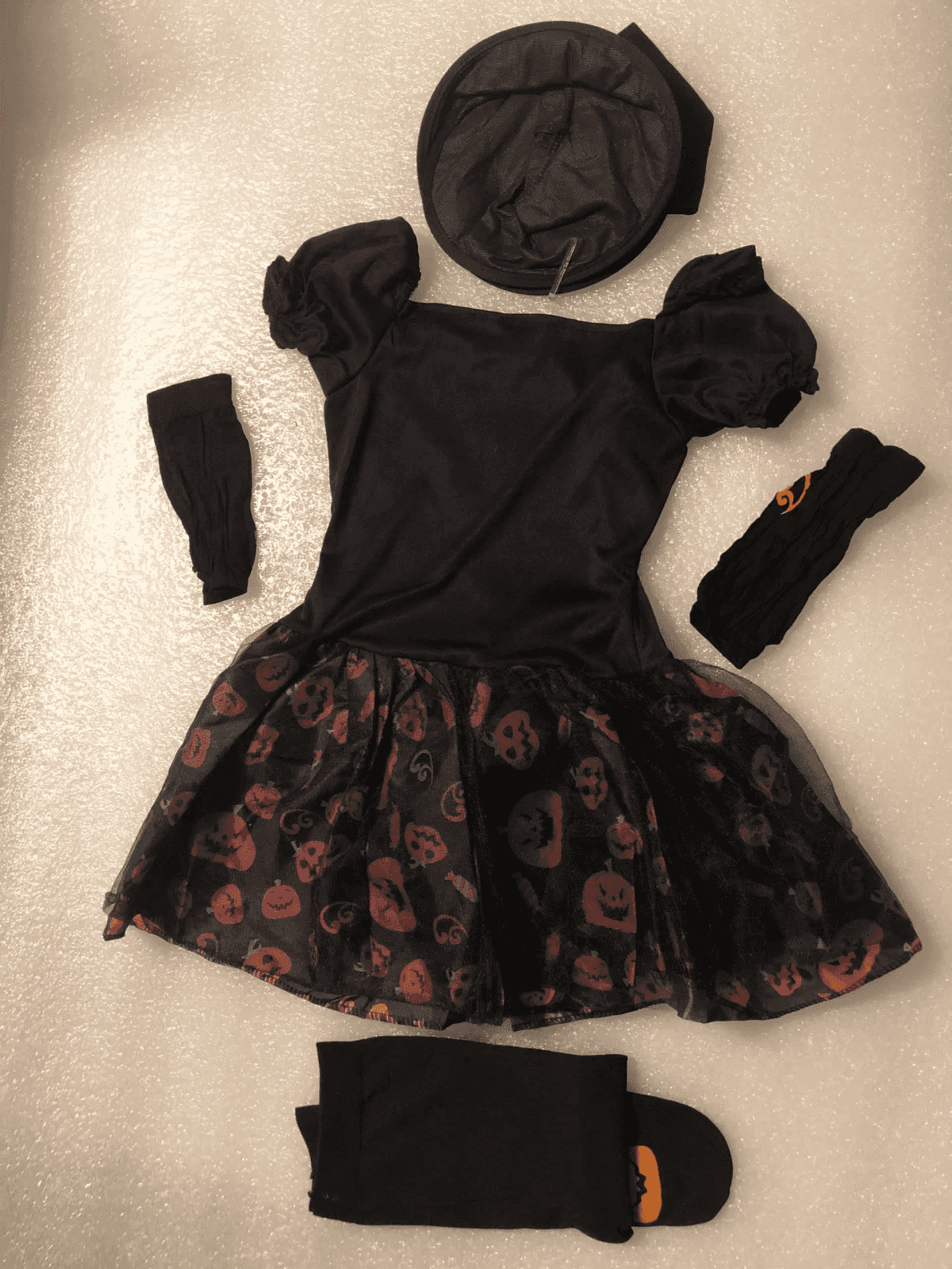 Un disfraz infantil de Halloween negro con estampado de calabazas, sombrero, medias y mangas sobre fondo brillante.