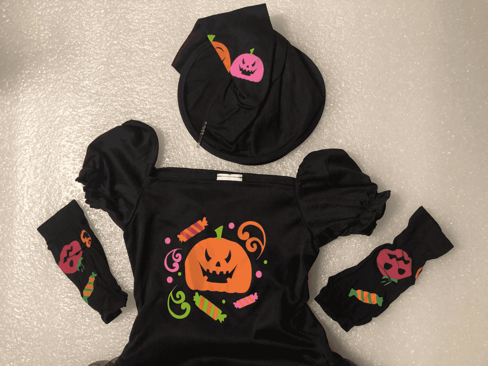 Un conjunto de disfraz de Halloween negro con sombrero, parte superior y mangas, decorado con calabazas y caramelos.