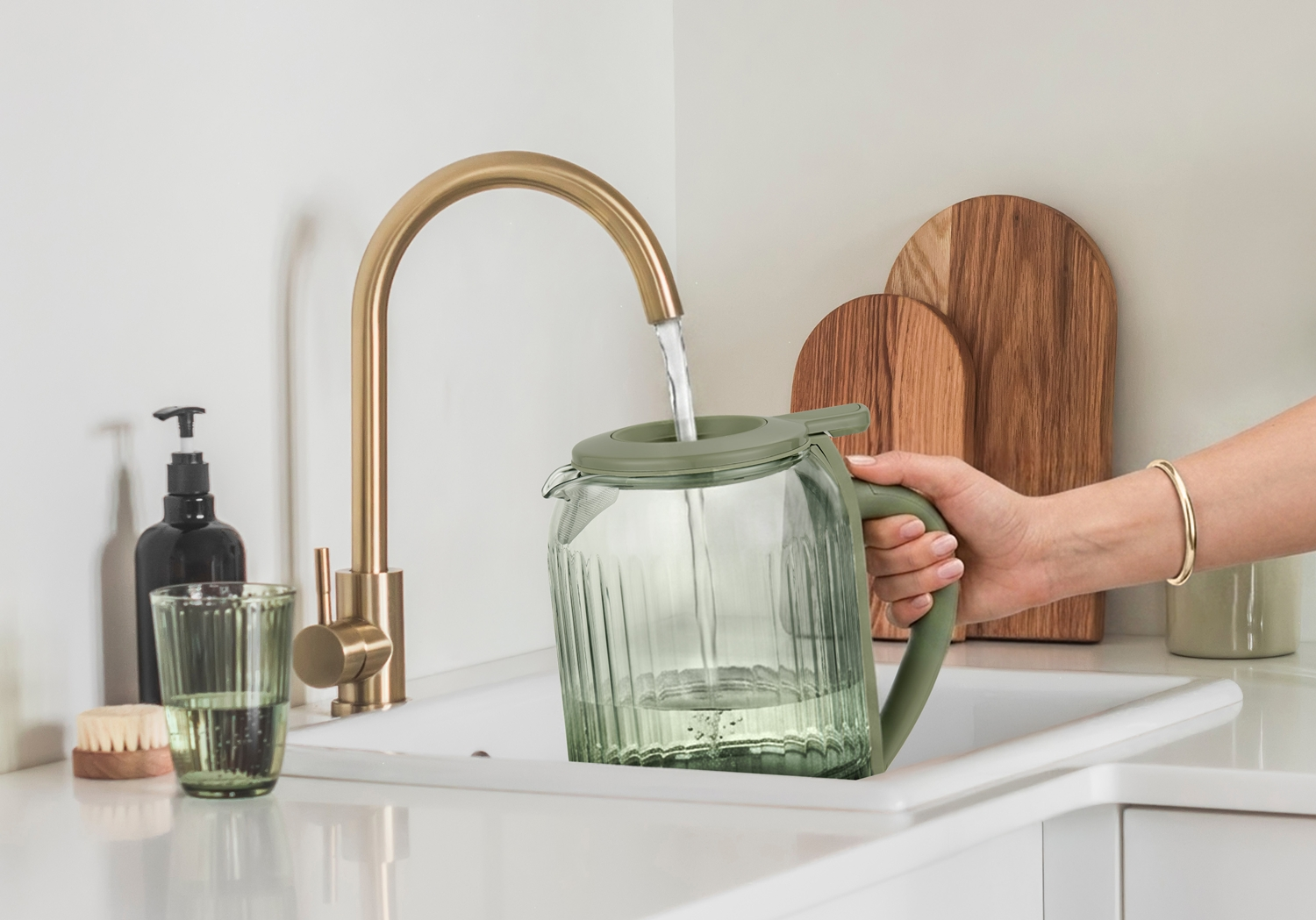 Una mano riempie una caraffa verde d'acqua da un rubinetto dorato in un lavandino.