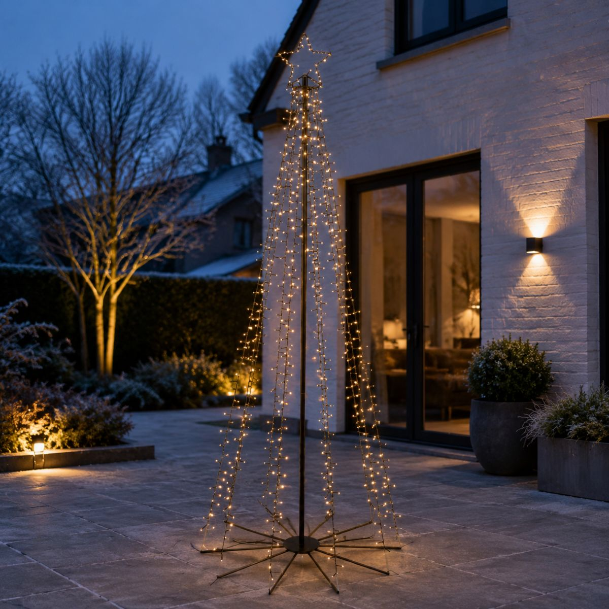 Beleuchteter Lichterketten-Weihnachtsbaum mit Sternspitze auf einer Terrasse im Garten bei Dämmerung.