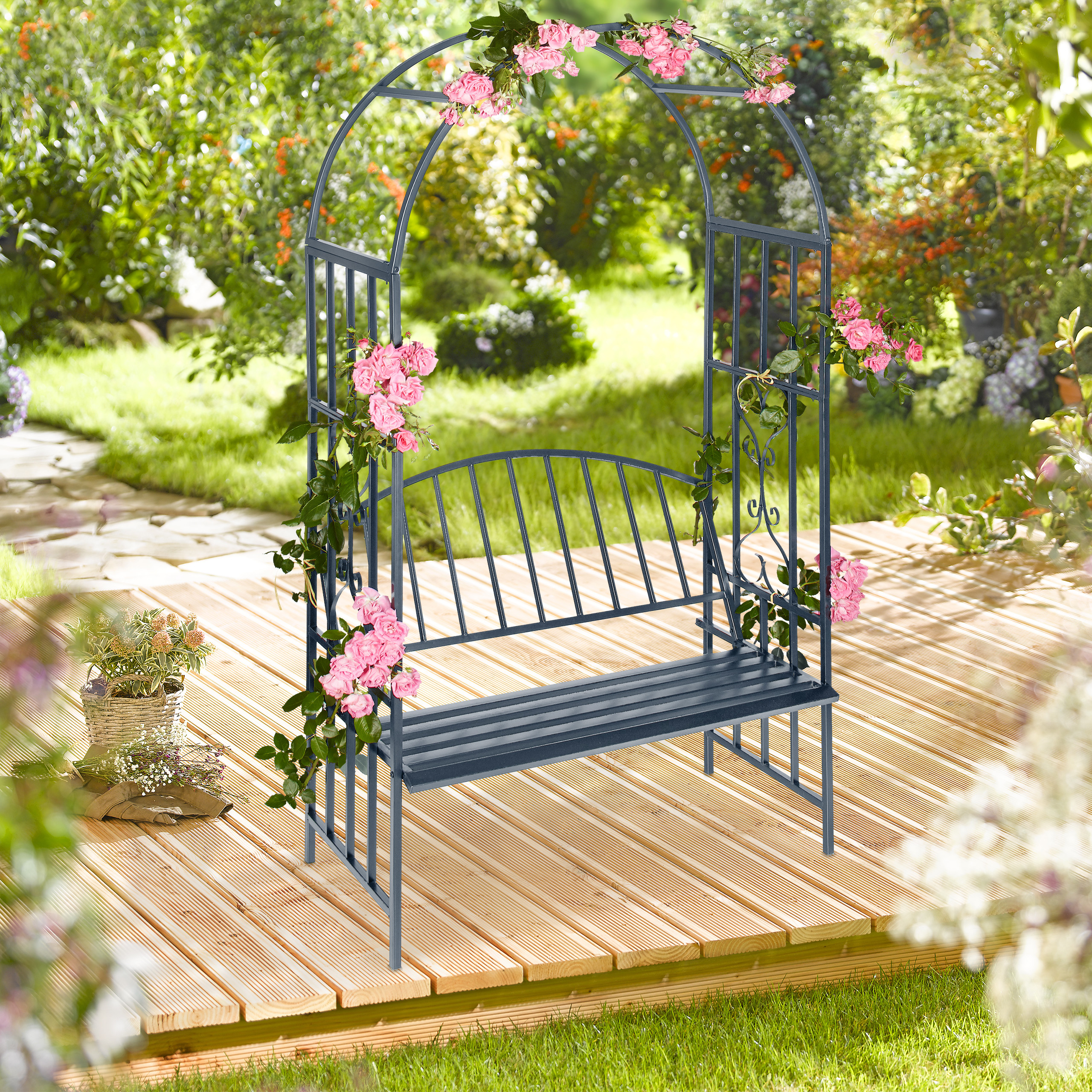 Eine dunkelgraue Gartenbank mit Rosenbogen auf Holzdeck im grünen Garten.