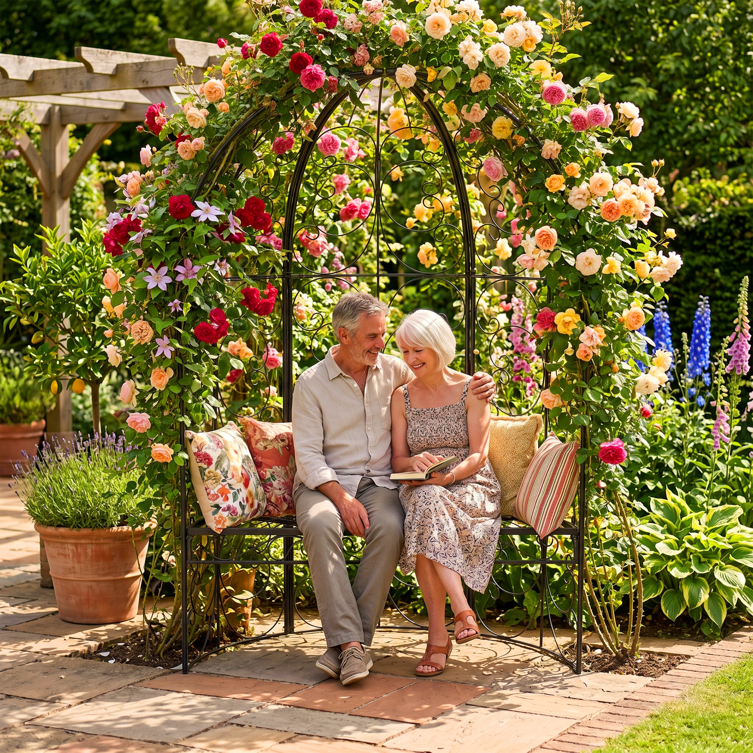 Ein älteres Paar sitzt auf einer Metallbank unter einem rosenbewachsenen Bogen und liest in einem sonnigen Garten.