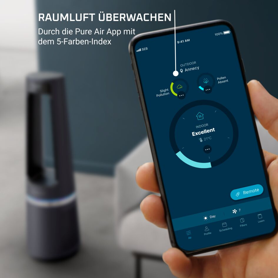 Ein Smartphone zeigt eine Luftqualitäts-App, im Hintergrund steht ein Luftreiniger.