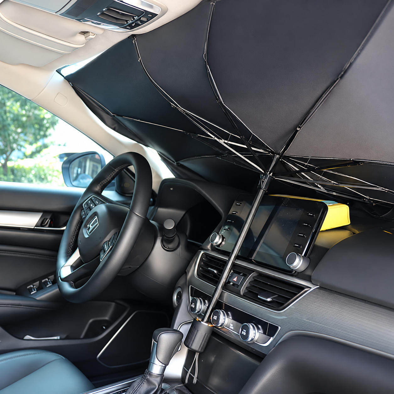 Ein offener, umgekehrter Regenschirm dient als Sonnenschutz an der Windschutzscheibe eines Autos.
